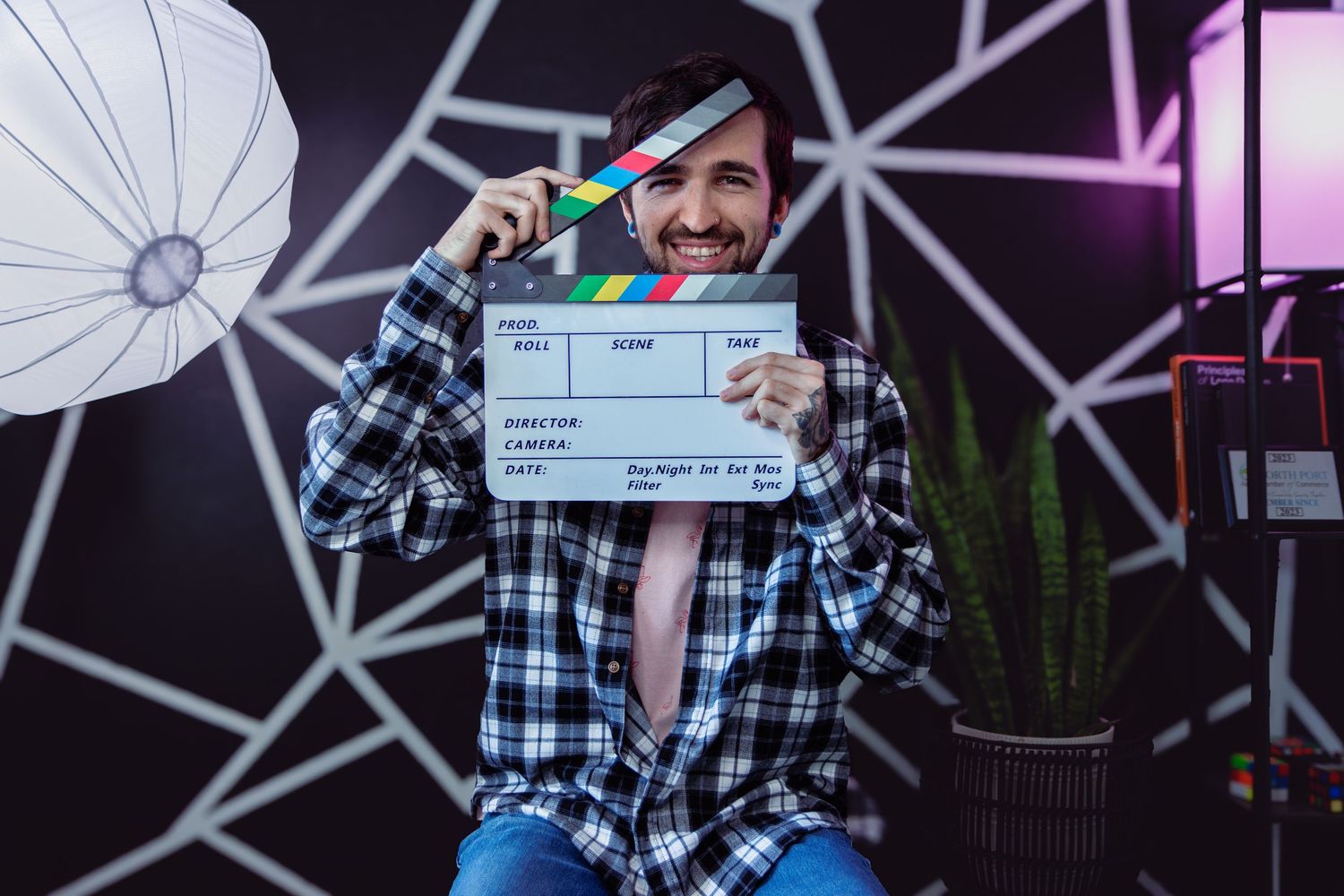 Person holding a film clapperboard in a photography studio with lighting equipment and geometric wall art.