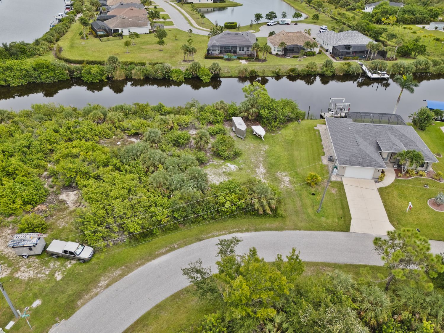 An aerial view of a residential neighborhood with houses, trees, and a pond surrounded by lush greenery.
