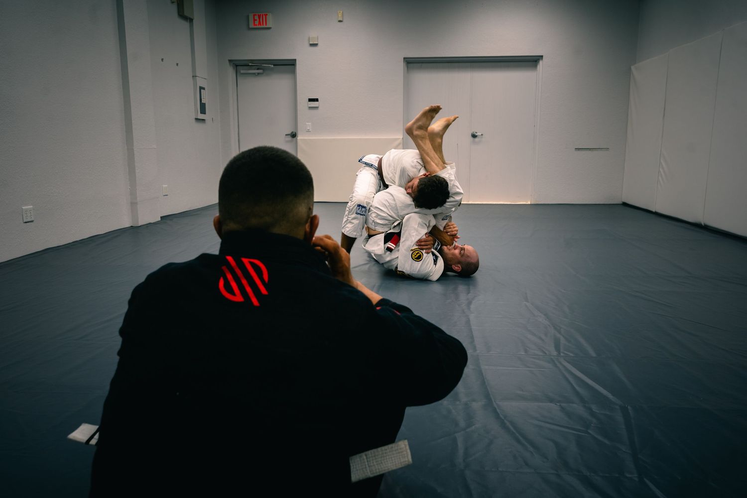 Dark training room or studio space with emergency exit signs visible.