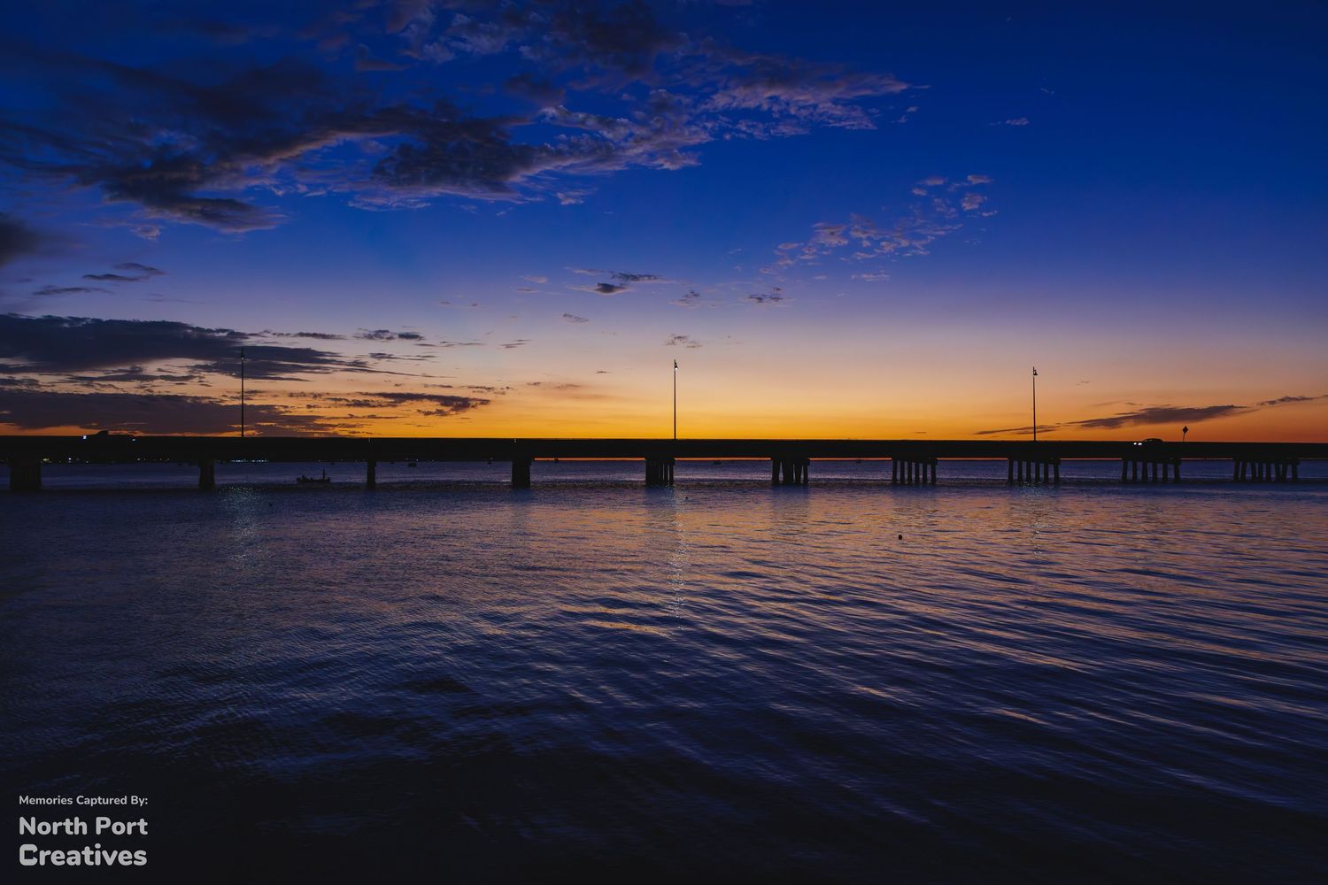 Stunning blue hour sunset over a long bridge reflecting on calm water, captured by North Port Creatives.