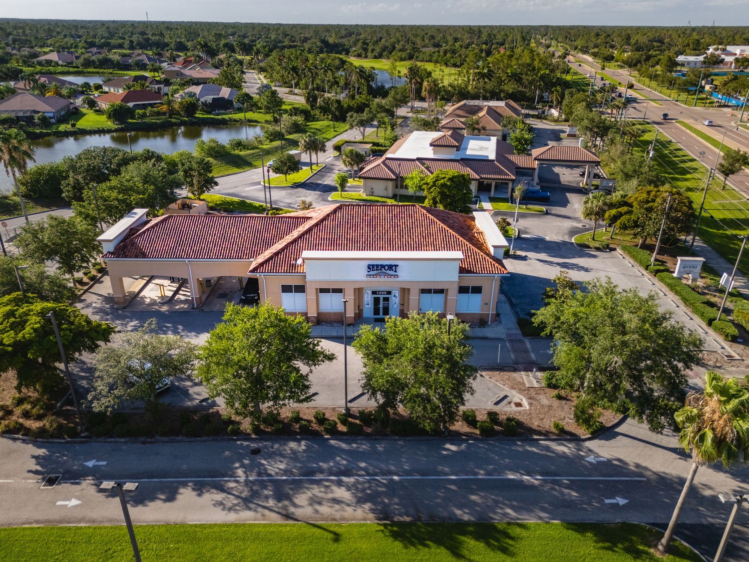 Aerial view of a commercial building with red tile roof surrounded by lush trees near a lake in a Florida suburb.