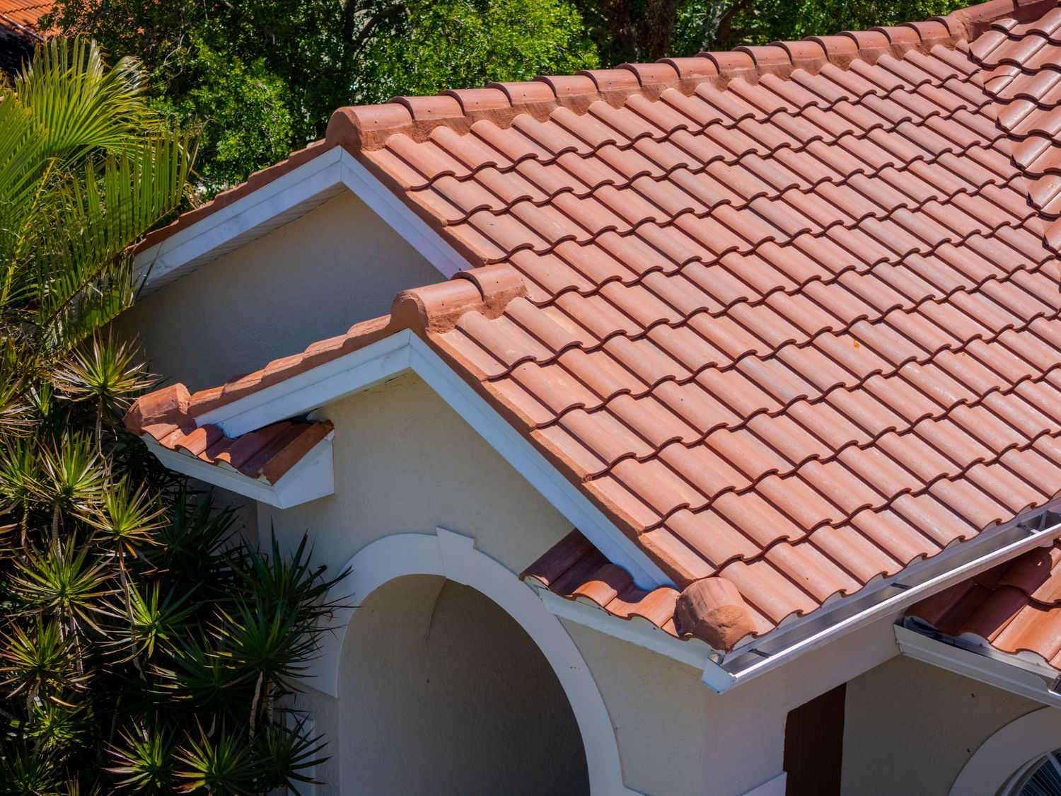 Close-up aerial view of a Mediterranean-style home featuring terracotta clay roof tiles with white stucco arches.