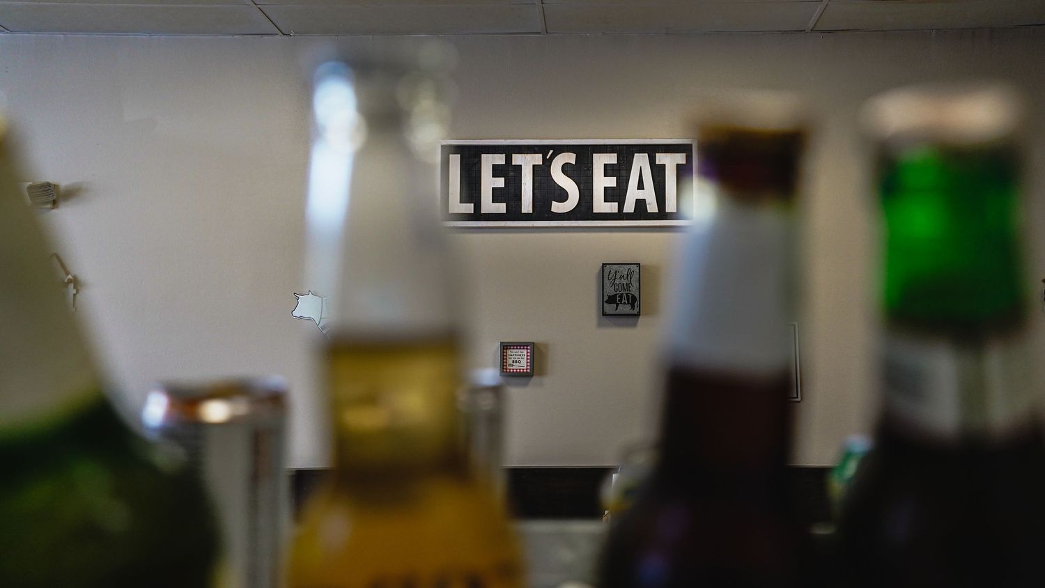 Illuminated 'LETS EAT' neon sign glowing in dark restaurant setting.