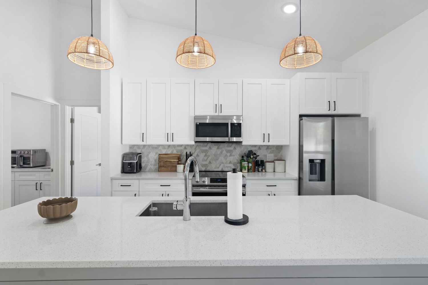 Modern white kitchen with quartz countertops, pendant lights, and stainless steel appliances shown from multiple angles.