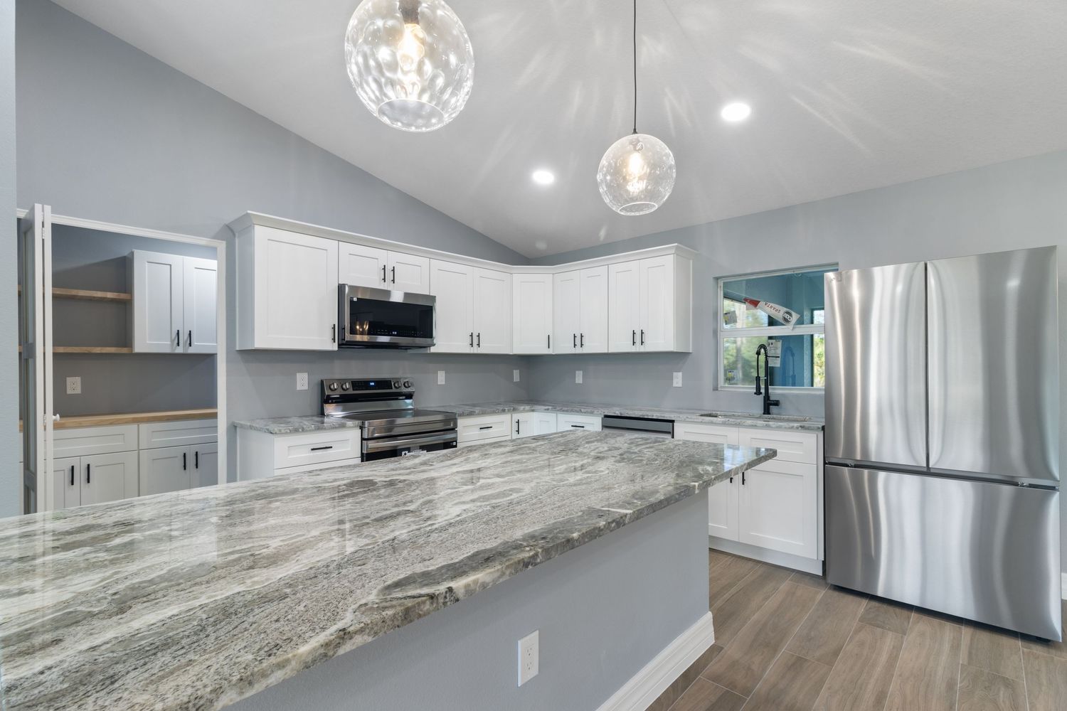 Modern kitchen interior with white cabinets, gray marble countertops, stainless steel appliances and pendant lighting.