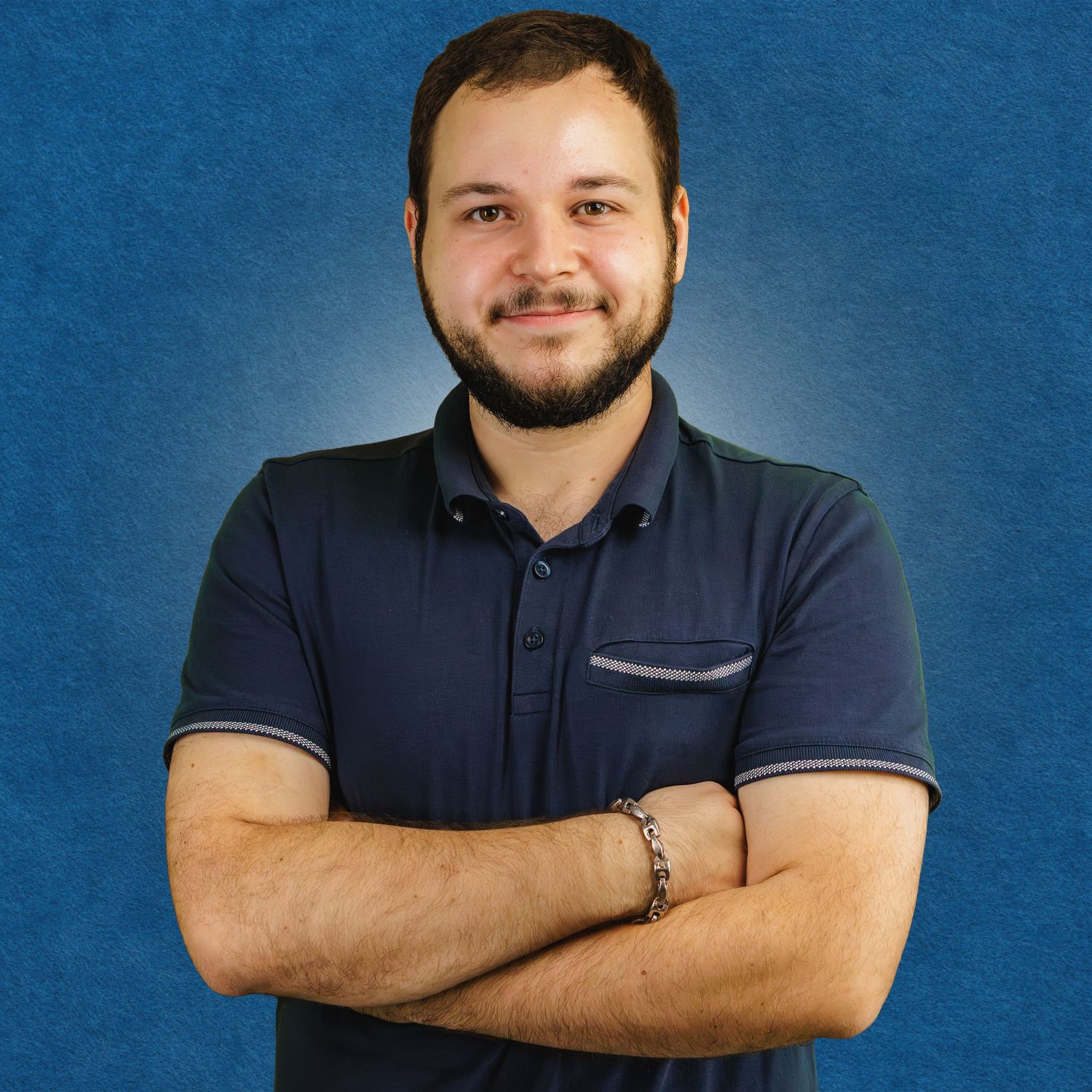 Professional headshot of someone in a navy polo shirt with crossed arms against a blue background.