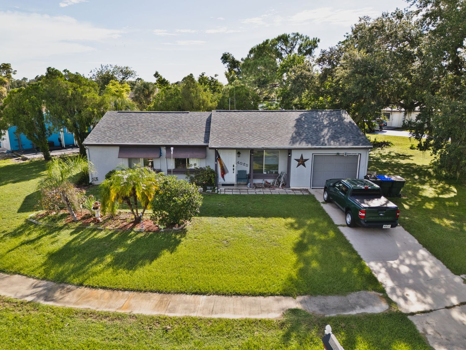 A large two-story gray house with a garage, surrounded by a well-manicured lawn and trees.