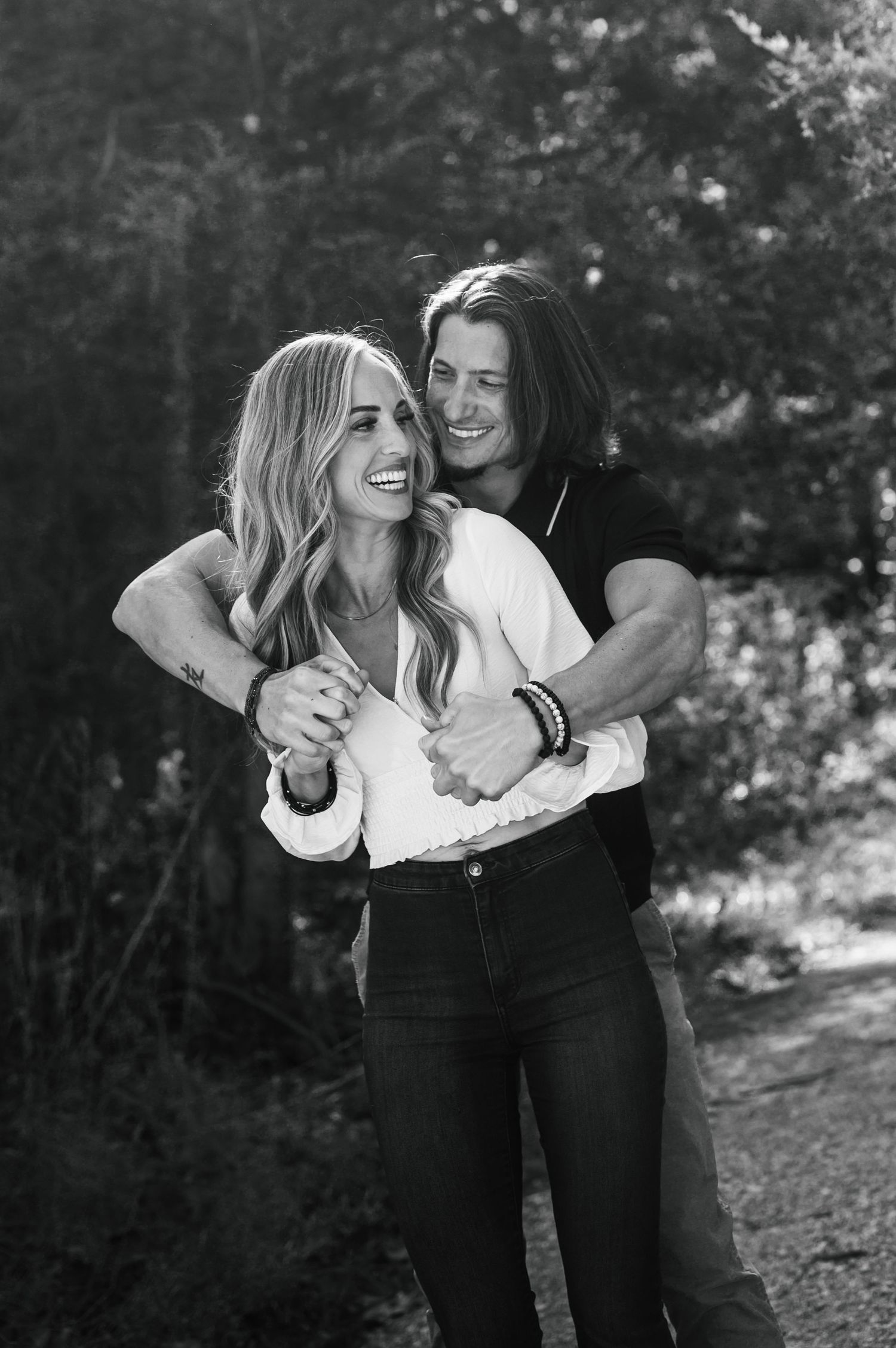 A couple shares a candid laughing moment together on a wooded path in black and white. Knoxville Couple Photographer