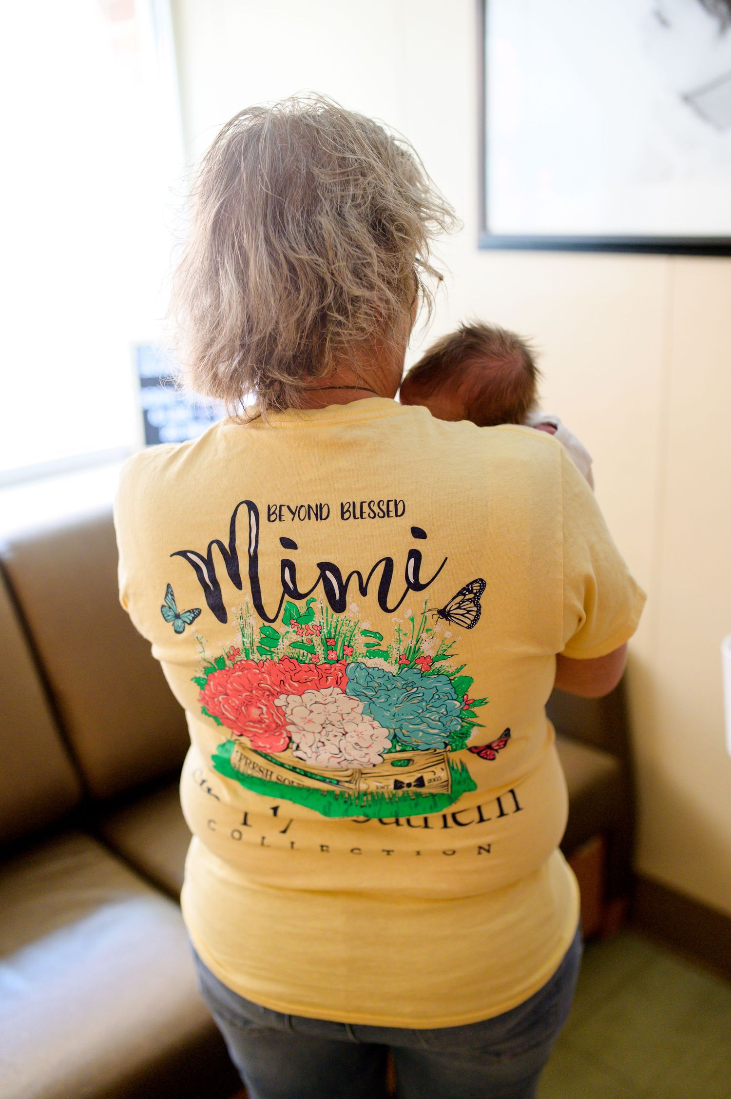 Person wearing yellow t-shirt with Miami design holds infant while sitting on leather couch. Knoxville Newborn Photographer UT Medical Cente