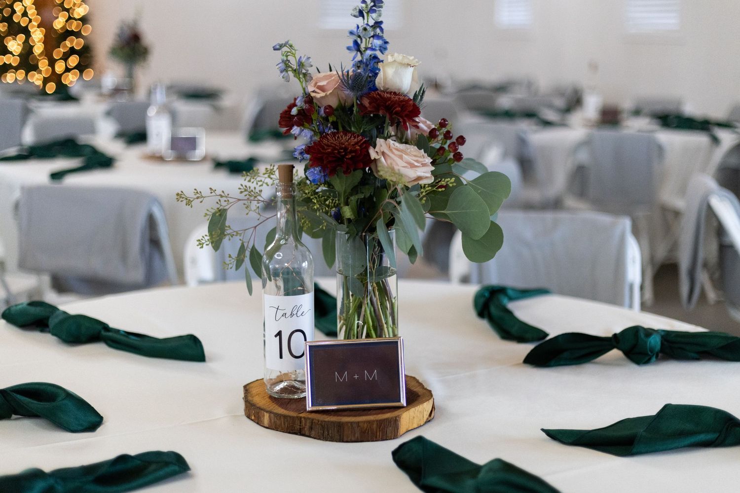 Elegant wedding reception table settings with emerald green napkins and floral centerpieces on wooden slices. Knoxville Wedding Photographer