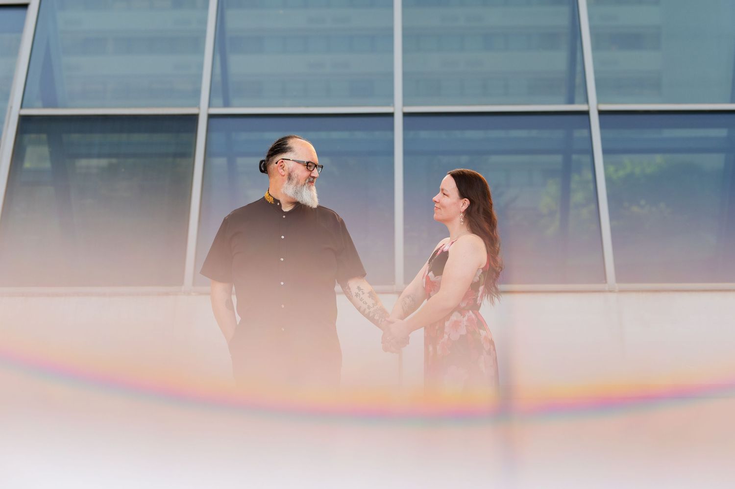 A romantic couple poses against a sleek glass building exterior. Knoxville Couple Photographer