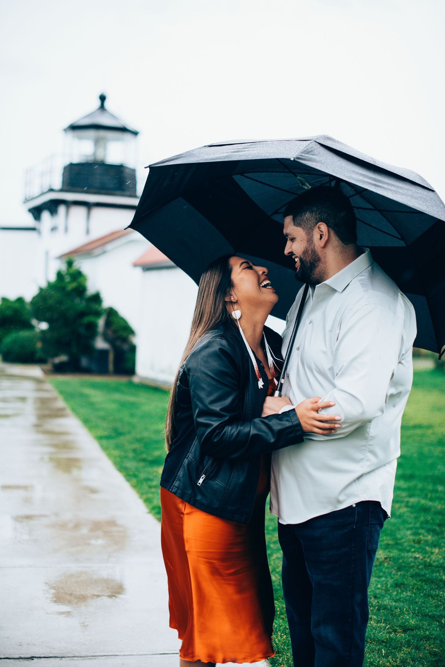 Couple sharing intimate moments under black umbrellas with lighthouse in background. Knoxville Couple Photographer