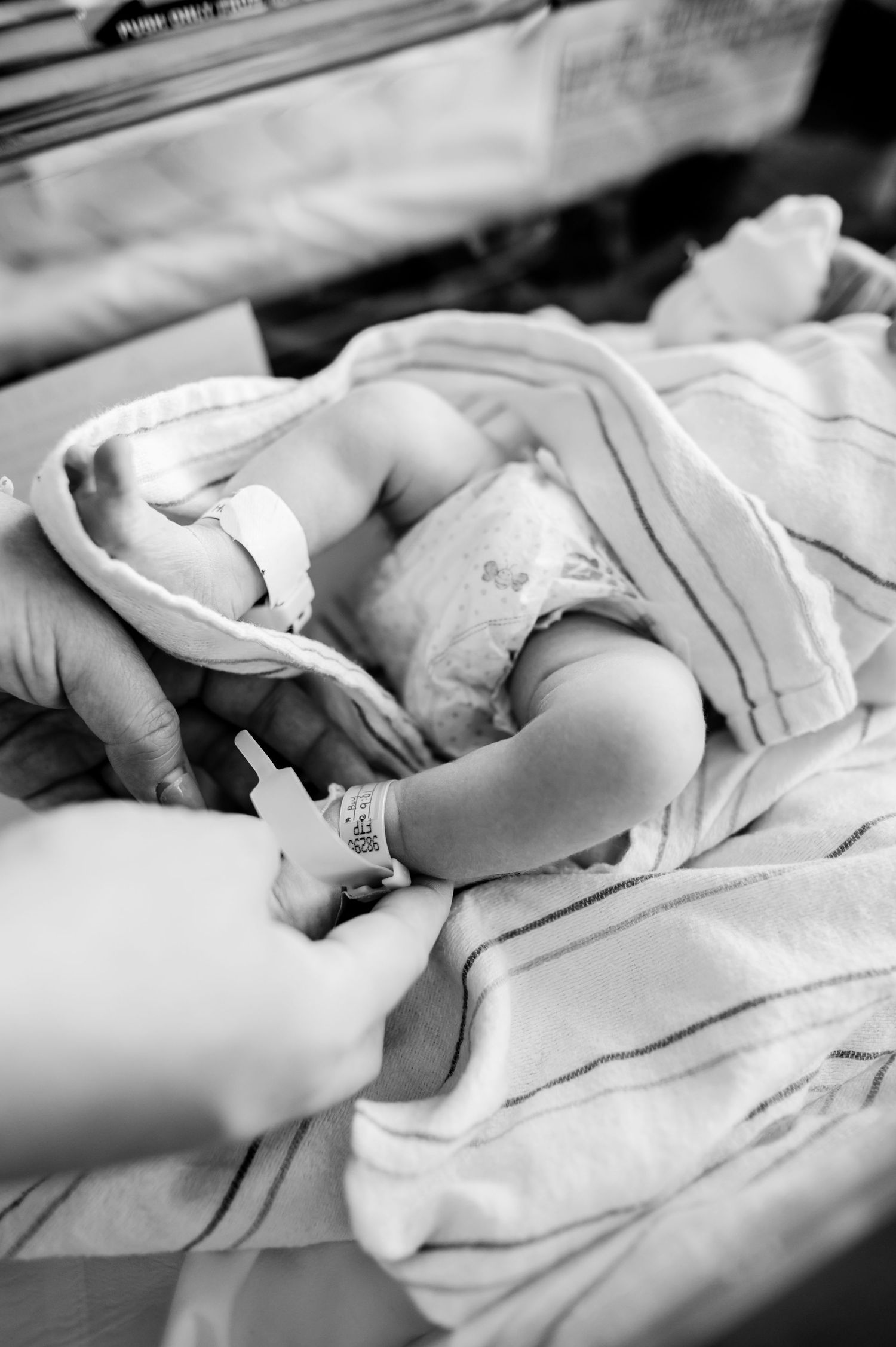 Gentle hands caring for a newborn wrapped in white hospital blanket. Knoxville Newborn Photographer UT Medical Center