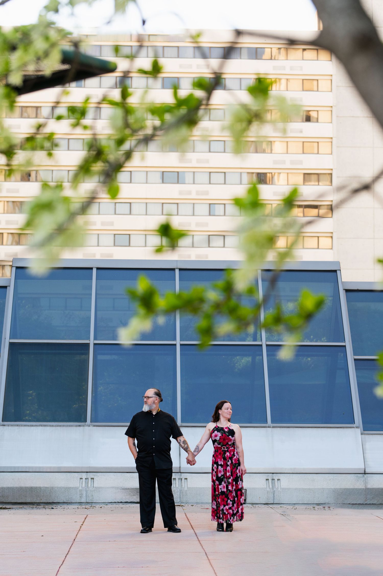 A couple stands together against a modern architectural backdrop with glass windows. Knoxville Couple Photographer. Market Square Knoxville