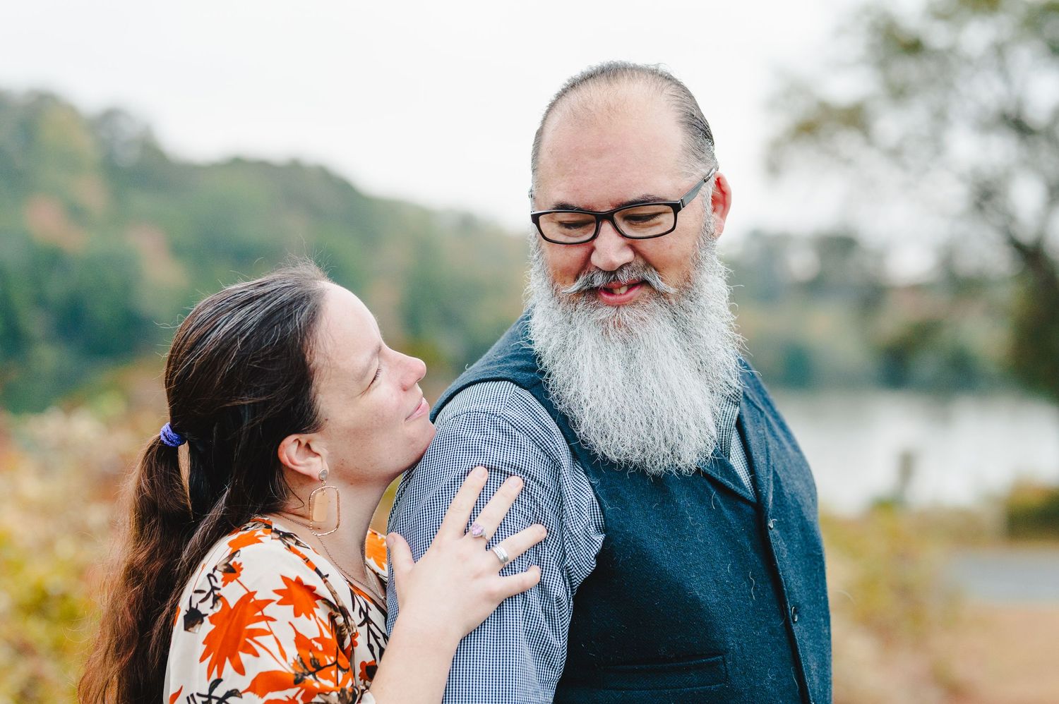 A couple laughs together during an intimate outdoor photo session with autumn colors behind them. Knoxville Couple Photographer. Melton Hill