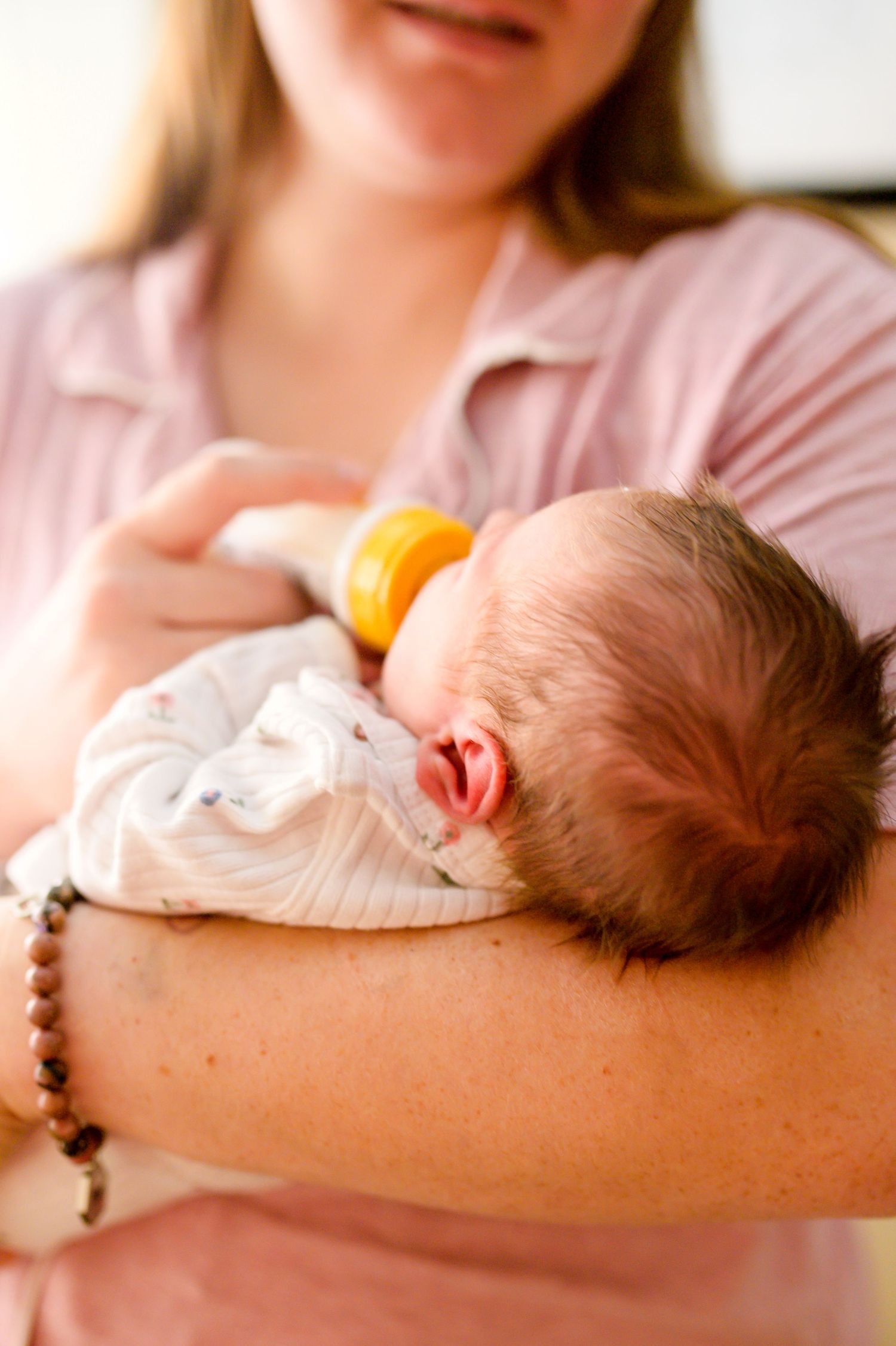 Baby sleeping on caregiver's arm while wearing white onesie. Knoxville Newborn Photographer