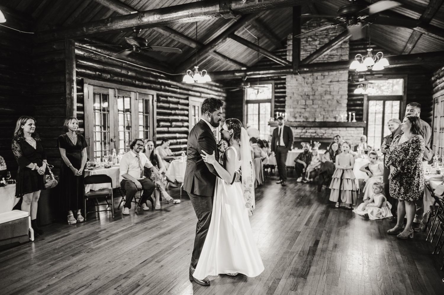 A wedding couple shares their first dance in a rustic log cabin venue surrounded by guests. Knoxville Wedding Photographer