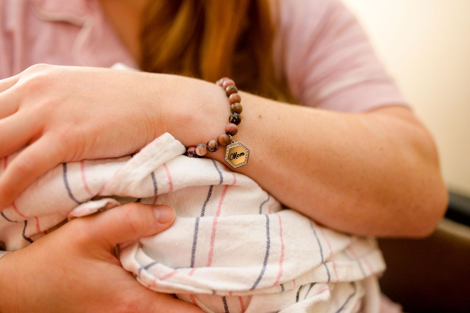 Close-up of hands wearing a beaded bracelet holding a swaddled infant. Knoxville Newborn Photographer