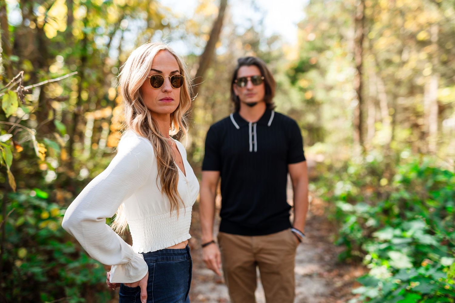 A stylish couple poses on a wooded trail wearing sunglasses and casual attire. Knoxville Couple Photographer
