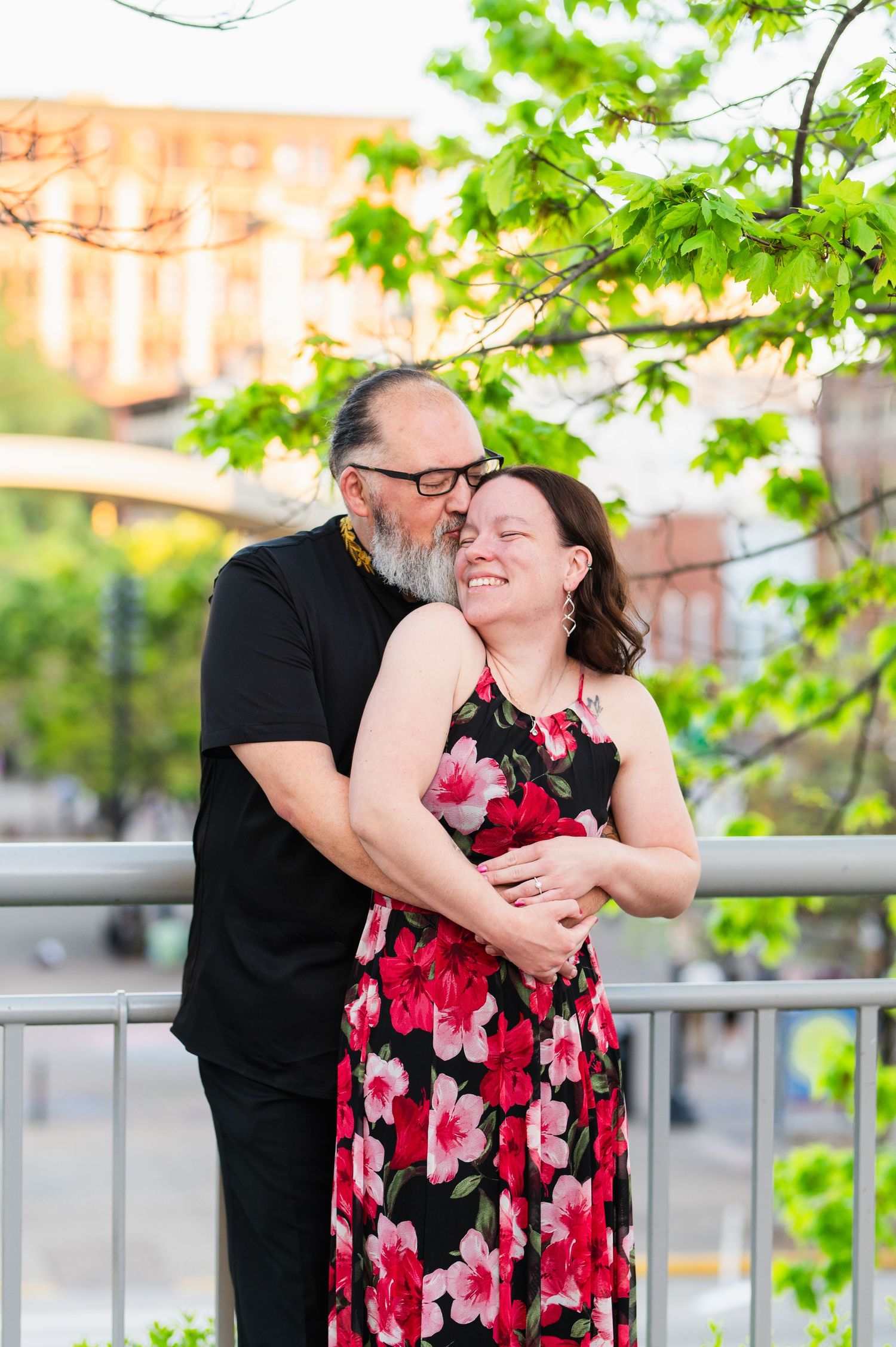 A couple embraces near a railing with green spring foliage in the background. Knoxville Couple Photographer