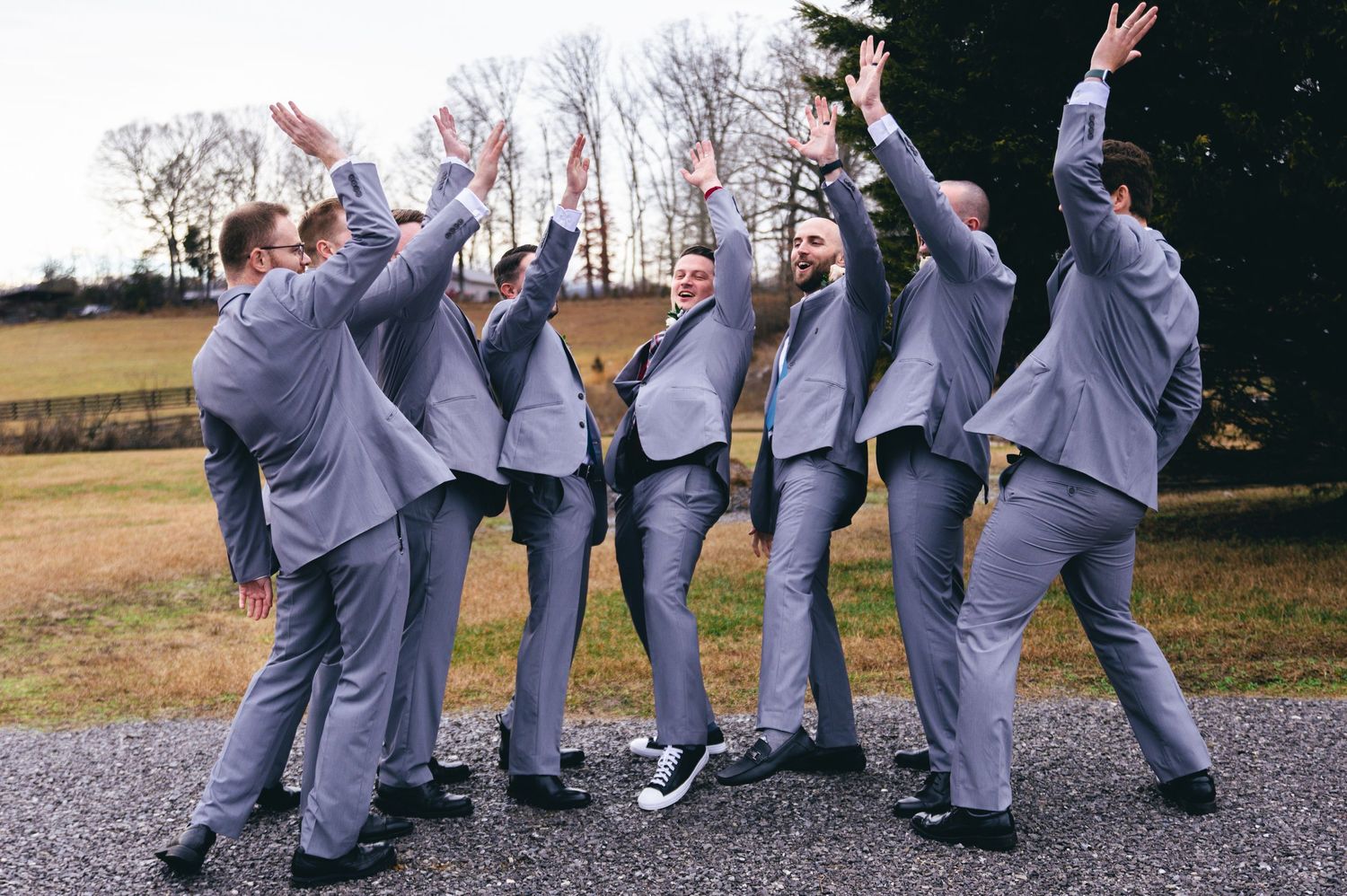 Wedding party in gray suits performs fun jumping poses for a group photo outdoors. Knoxville Wedding Photographer