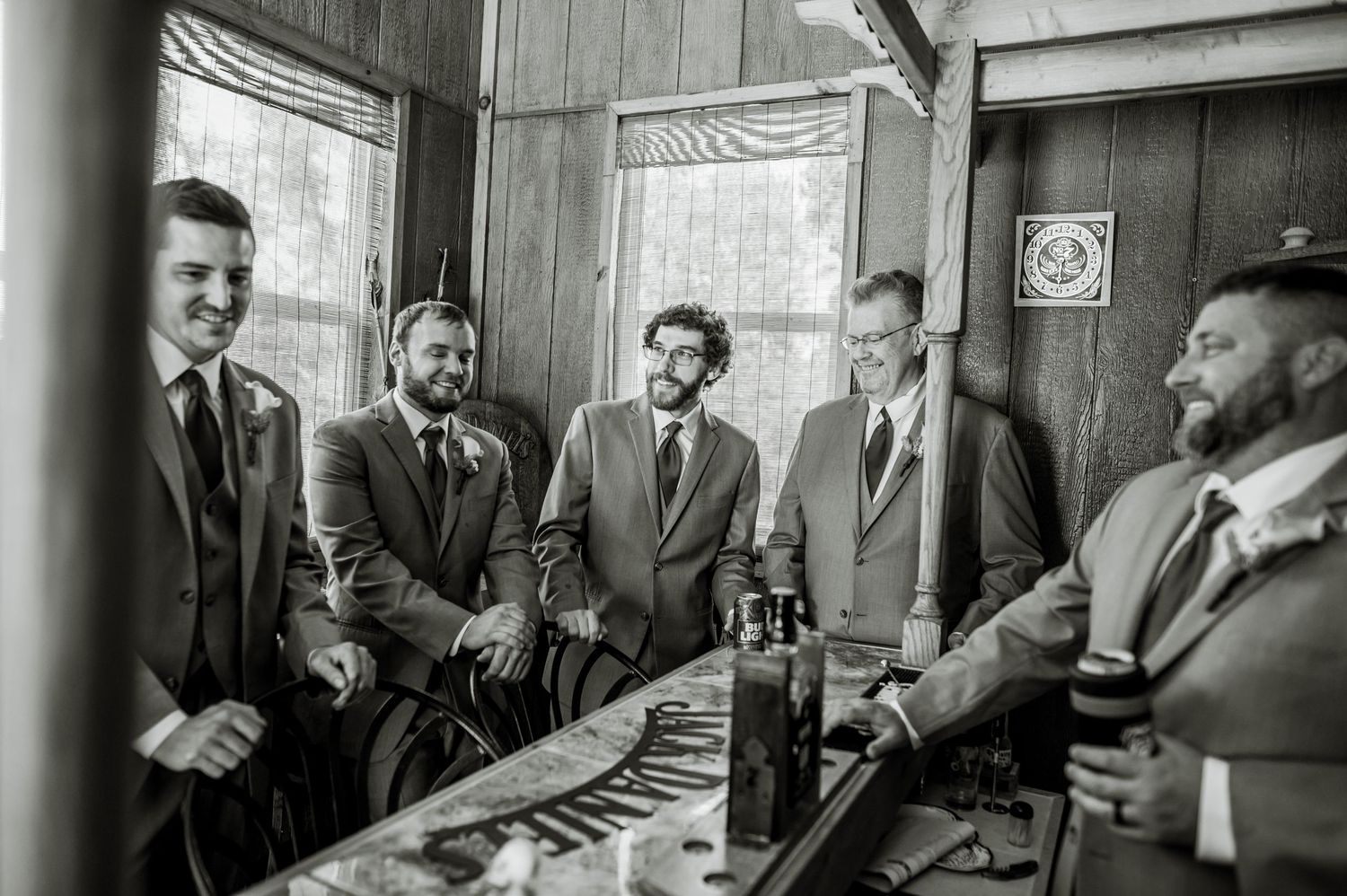 Groomsmen in suits share laughs and conversation in a rustic wooden room. Knoxville Wedding Photographer