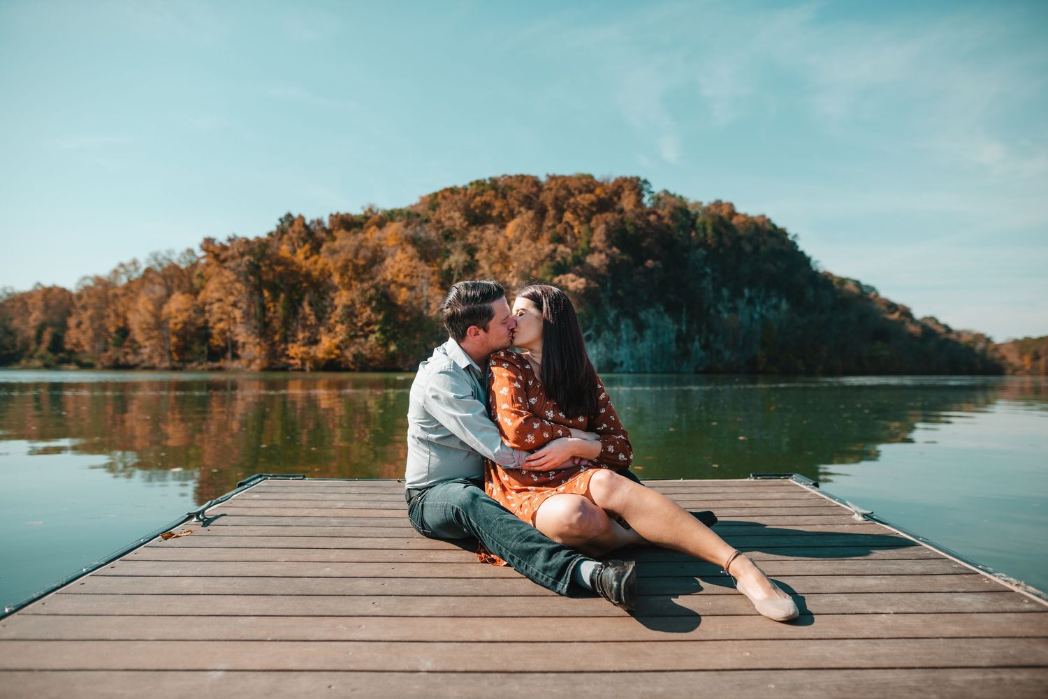 A couple sits intimately on a wooden dock with a scenic autumn lake view. Knoxville Couple Photographer. Melton Hills Park