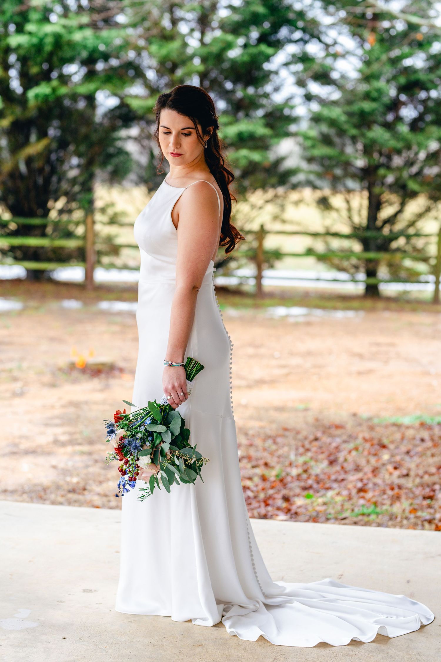 A bride in an elegant white dress holds a colorful bouquet while posing outdoors. Knoxville Wedding Photographer