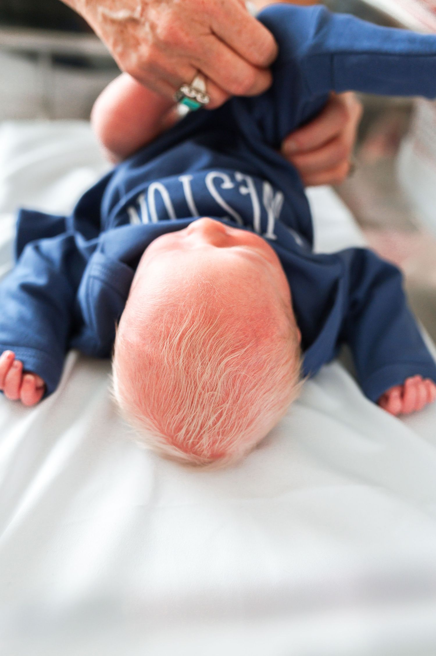 Newborn wearing navy blue outfit resting on white hospital bedding. Knoxville Newborn Photographer