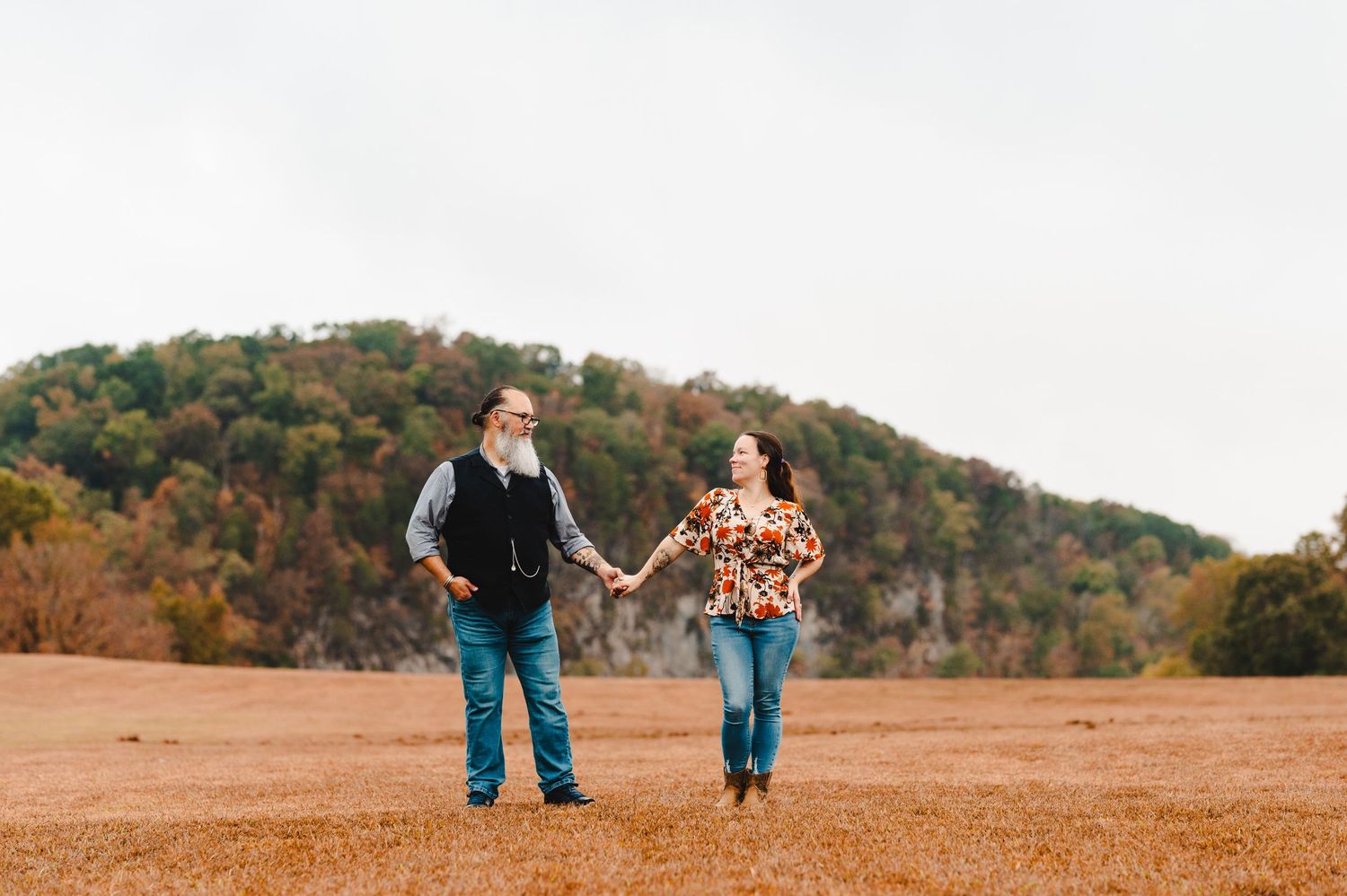 A couple holds hands while walking together in a scenic fall landscape. Knoxville Couple Photographer