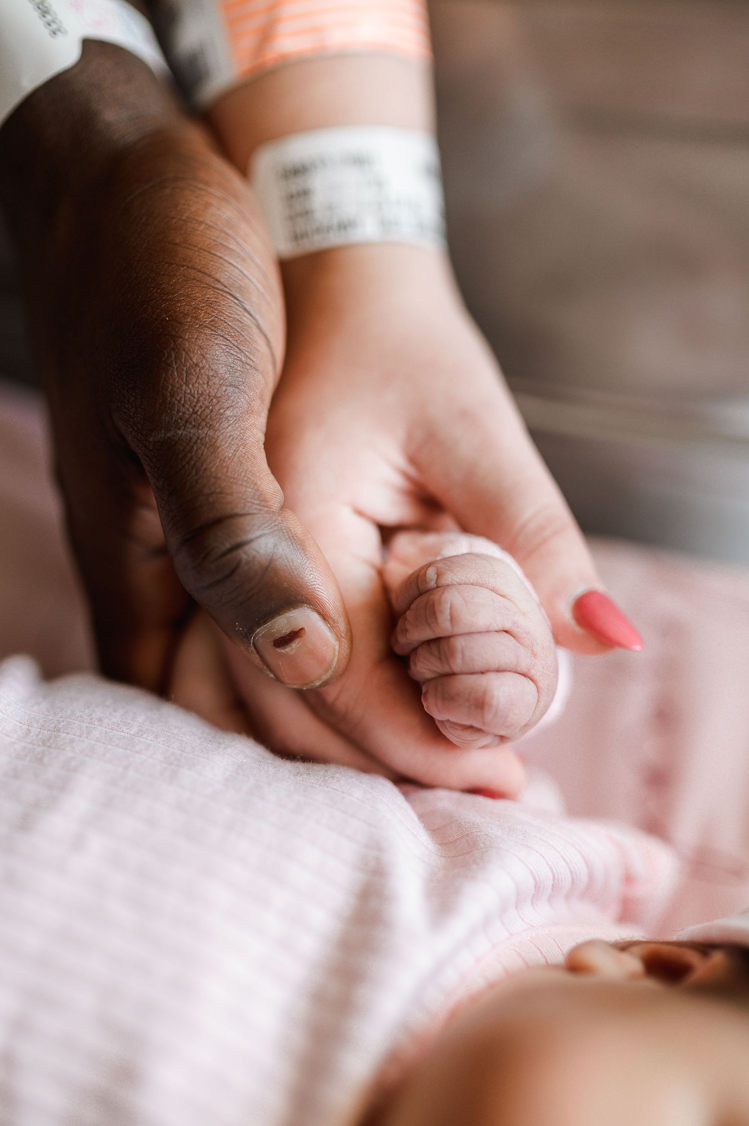 Close-up view of hands holding a newborn baby's tiny fingers against pink fabric. Knoxville Newborn Photographer