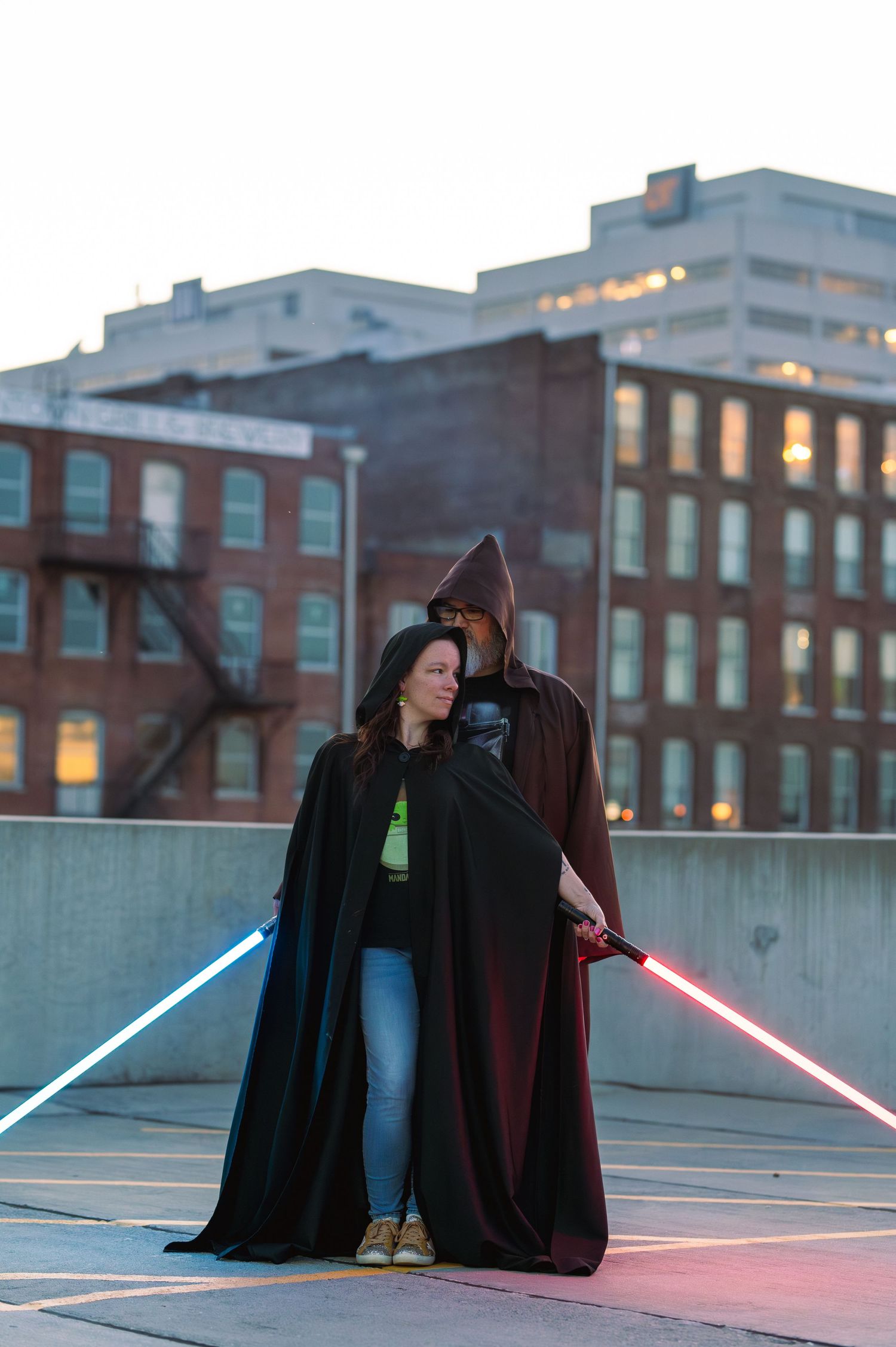 A couple dressed in Star Wars costumes with lightsabers on a rooftop at dusk. Knoxville Couple Photographer