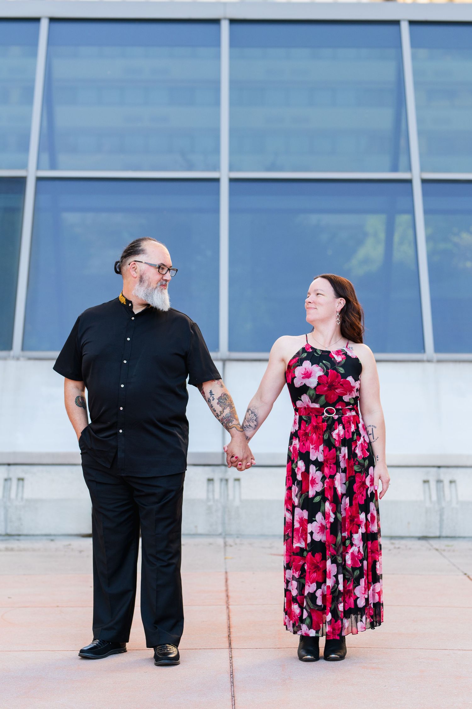 A couple in contrasting outfits posing against a modern glass building facade. Knoxville Couple Photographer