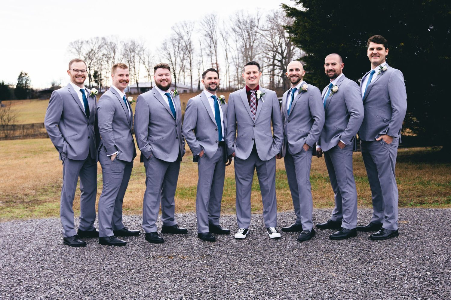 Groomsmen in matching gray suits pose together on a gravel path during an outdoor wedding celebration. Knoxville Wedding Photographer