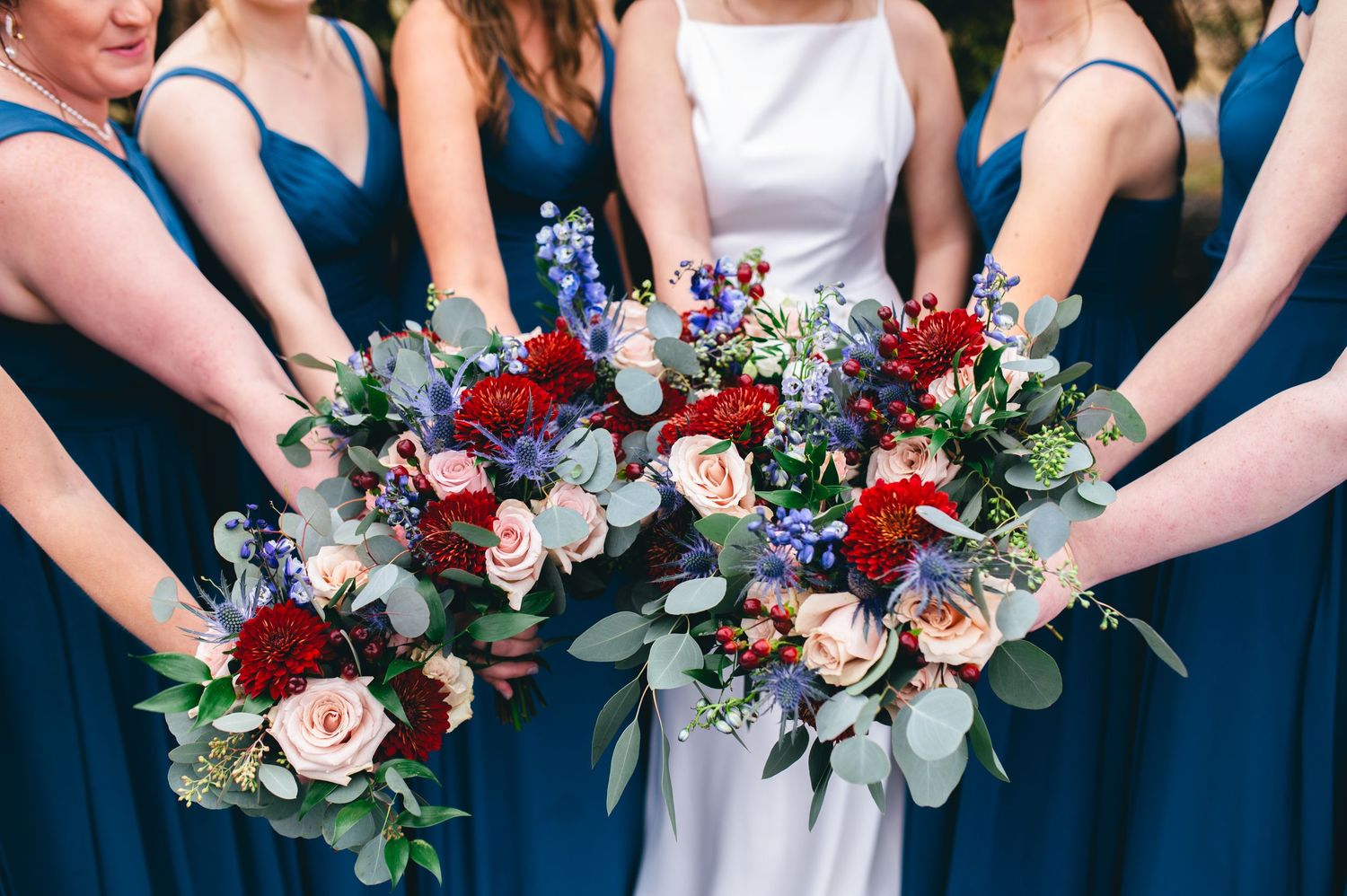 Bridesmaids in blue dresses hold colorful bouquets featuring red and white flowers. Knoxville Wedding Photographer