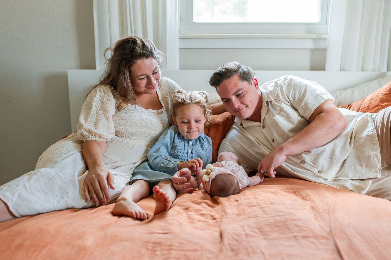 Family lounging together on a cozy bed with white linens during a relaxed morning at home.
