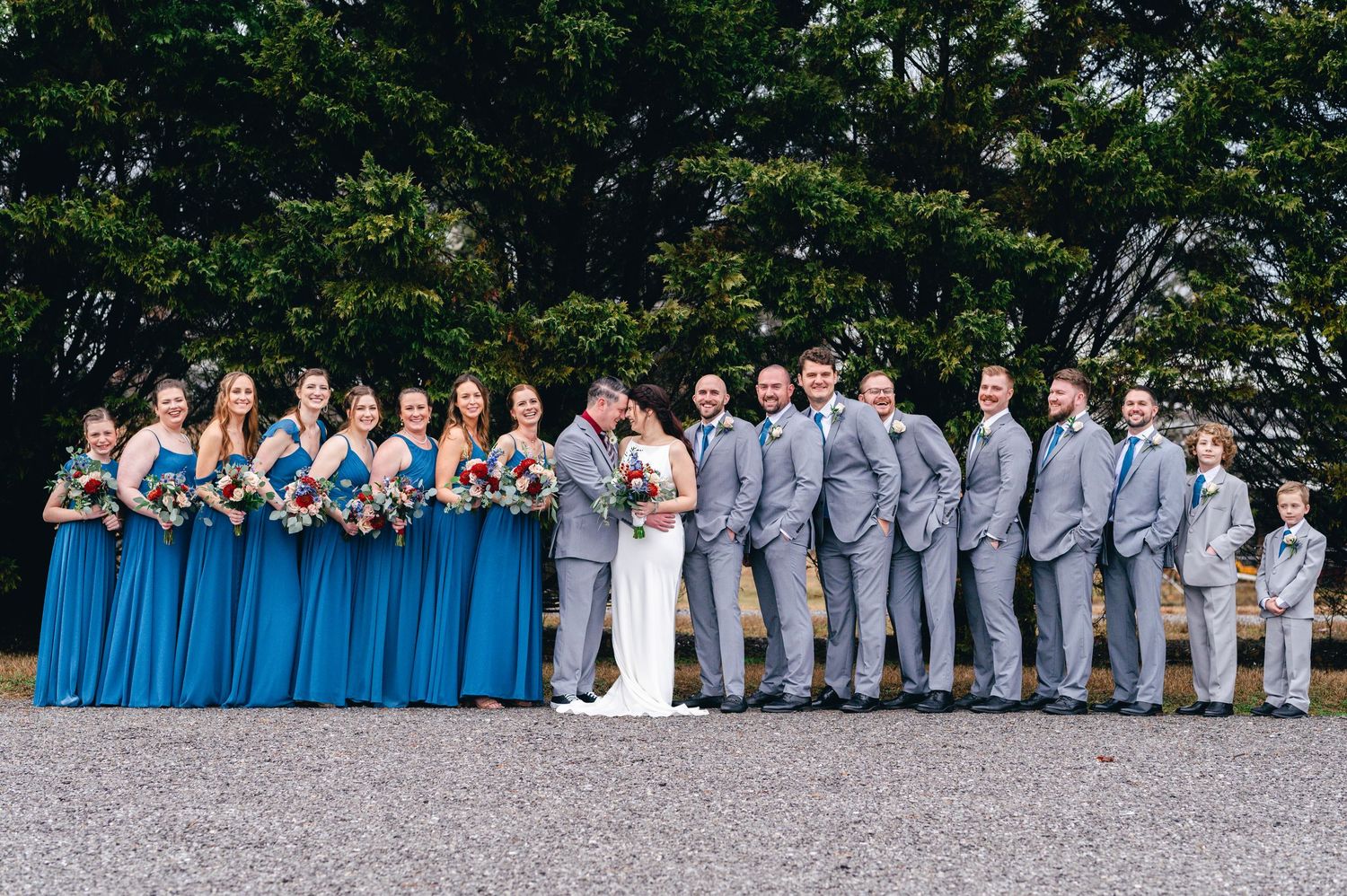 Wedding party in blue dresses and grey suits poses together on a gravel path. Knoxville Wedding Photographer