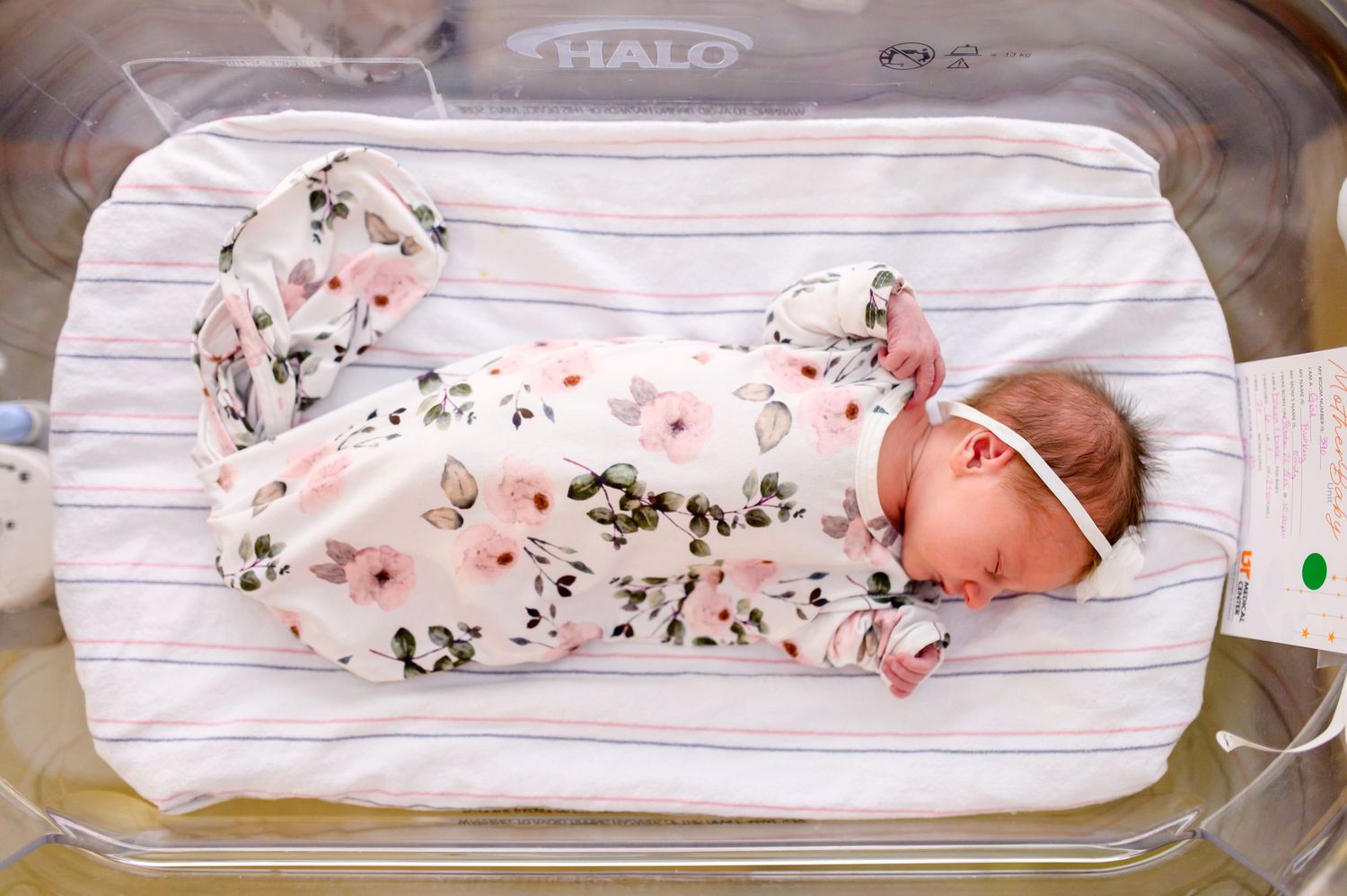 Newborn baby wearing floral outfit sleeping in hospital bassinet. Knoxville Newborn Photographer