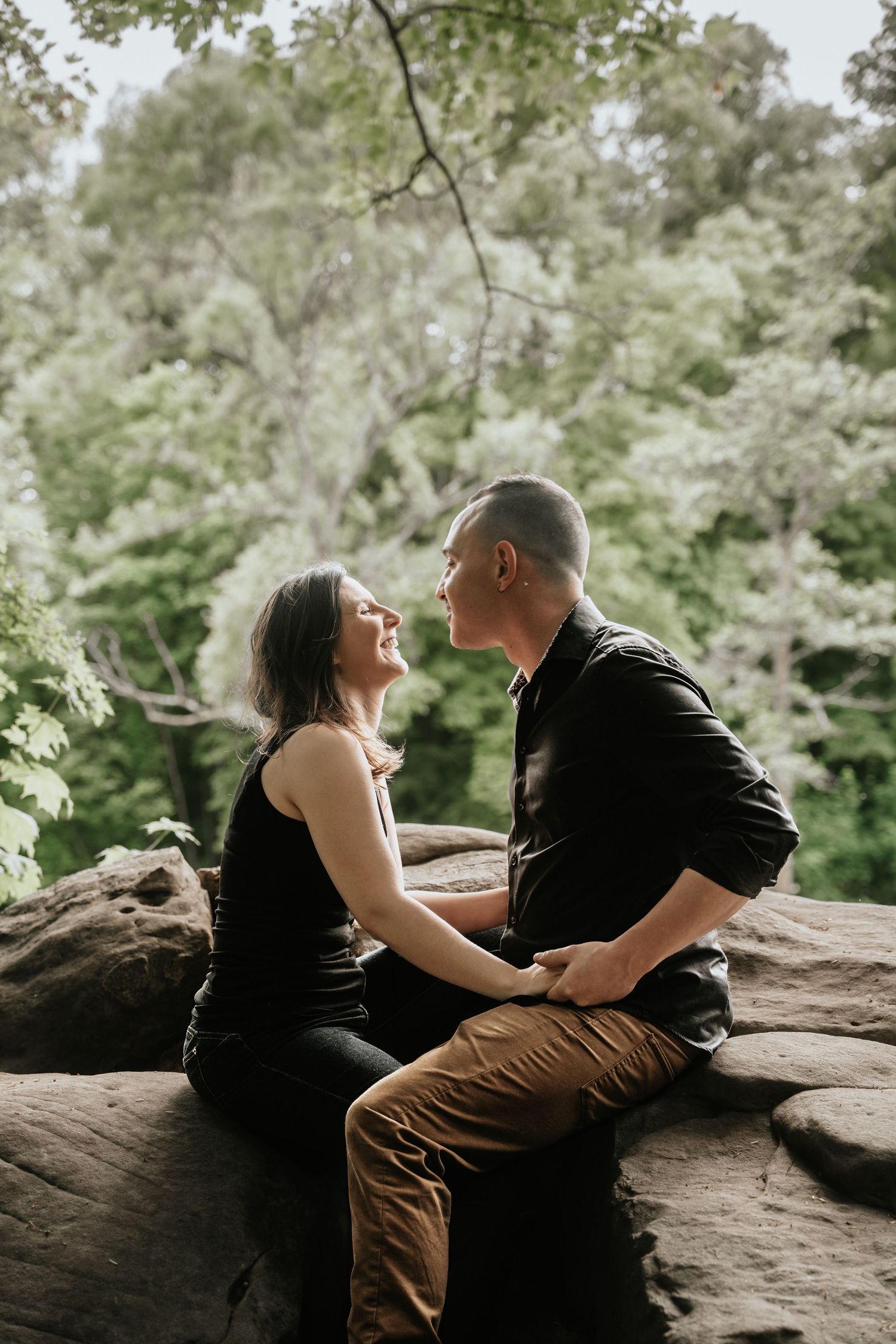 A couple shares intimate moments while relaxing on large rocks in a natural outdoor setting.