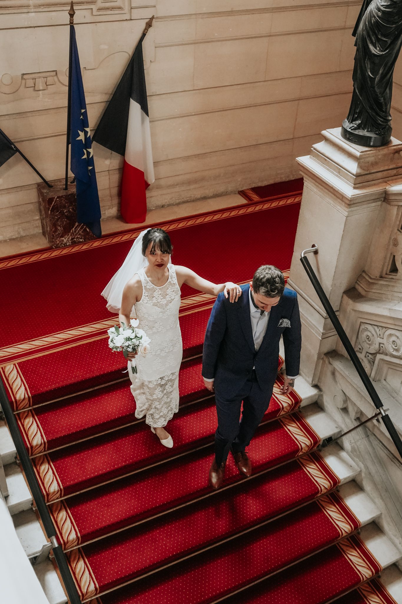 Un couple descendant d'élégants escaliers à tapis rouge en tenue de mariage formelle.