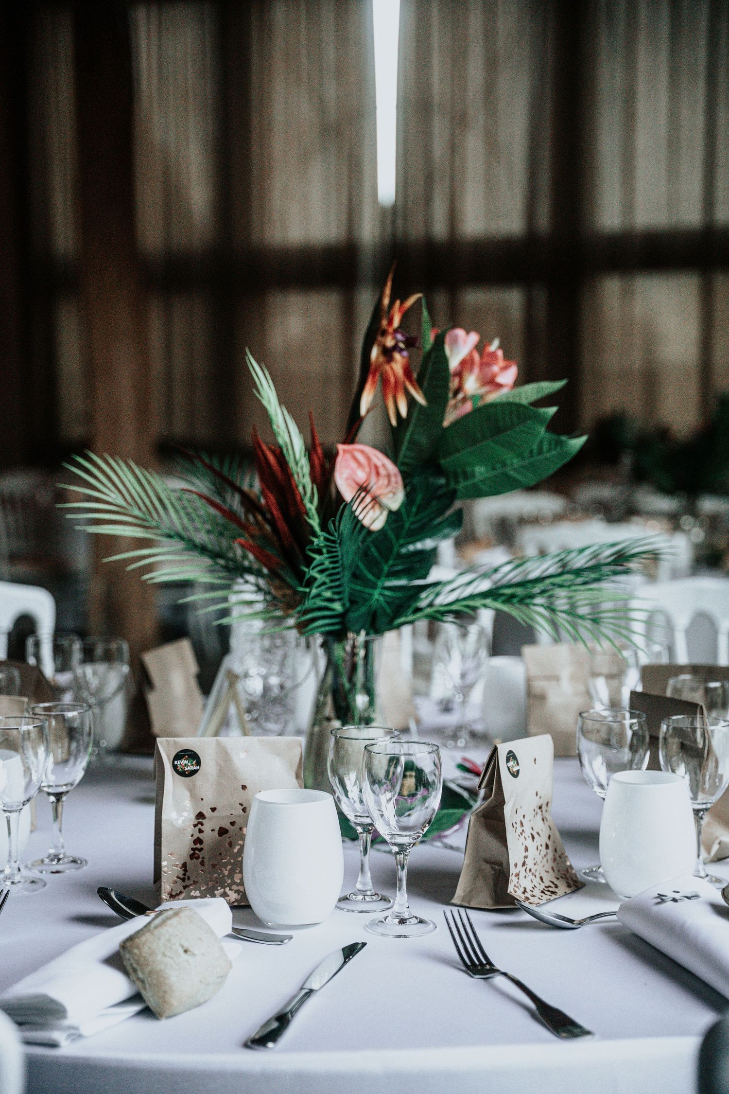 Cadre de table élégant avec des centres de table de verdure tropicale et des espaces de table formels lors de la réception de mariage.