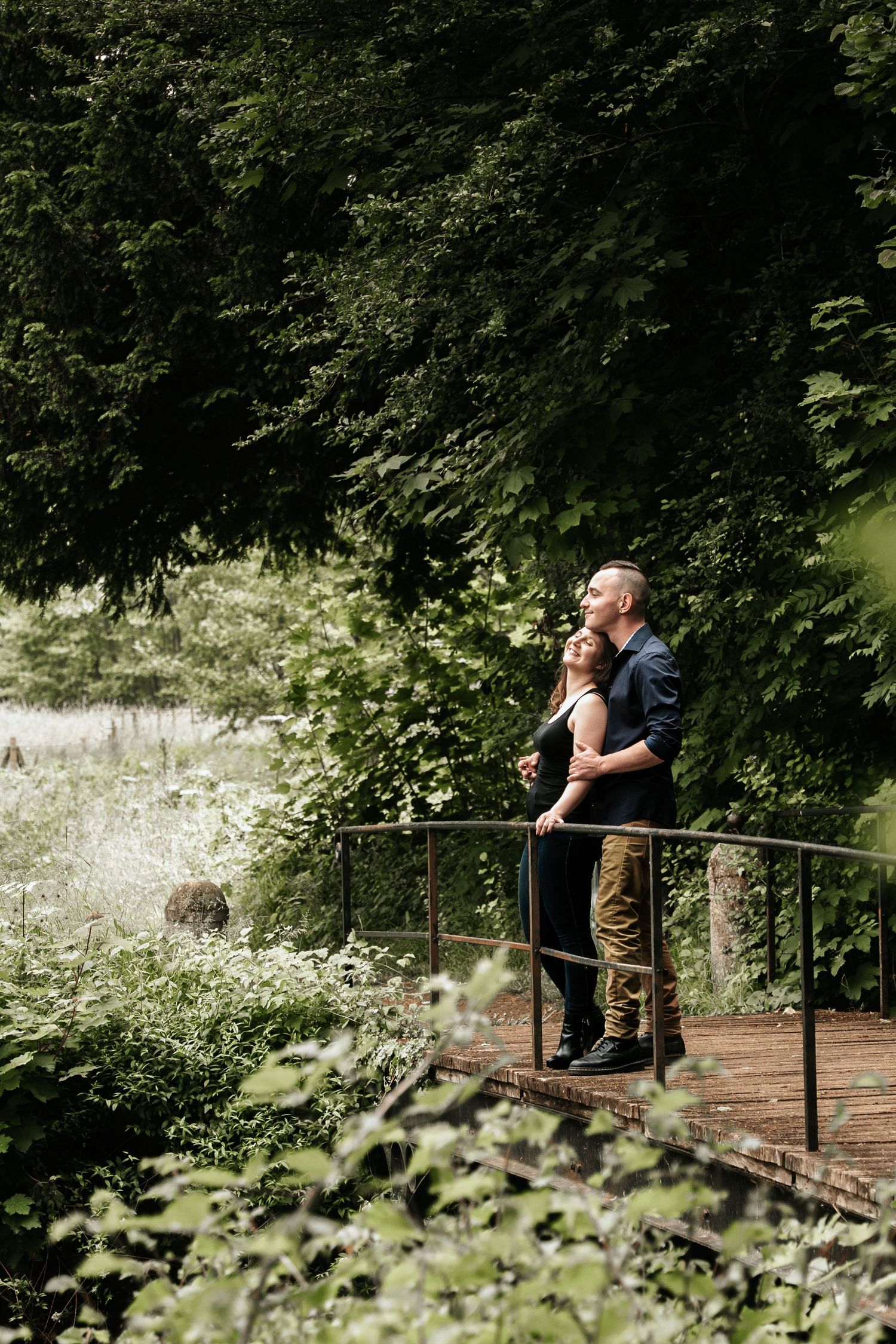 Un couple partageant un moment complice sur un pont rustique entouré d'une verdure luxuriante.