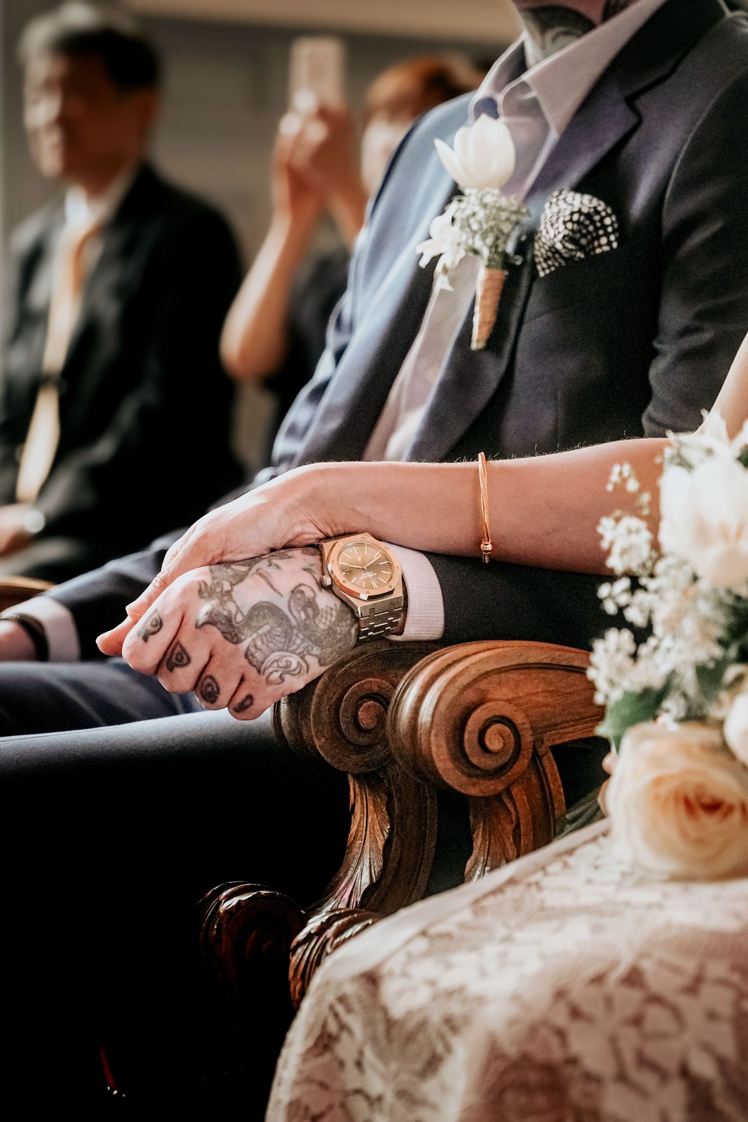 Plan détaillé de deux mains entrelacés sur des chaises vintage lors d'une cérémonie de mariage formelle.