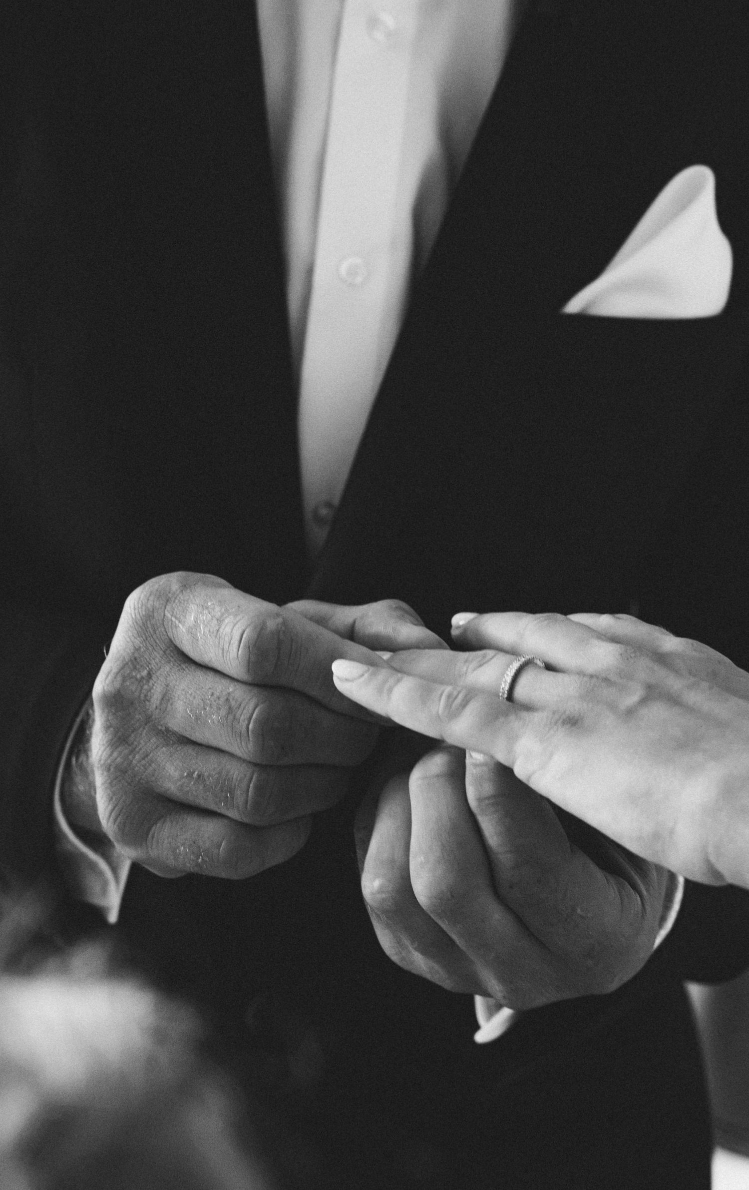 Black and white photo of a groom placing a wedding ring on his bride's finger during a wedding ceremony.