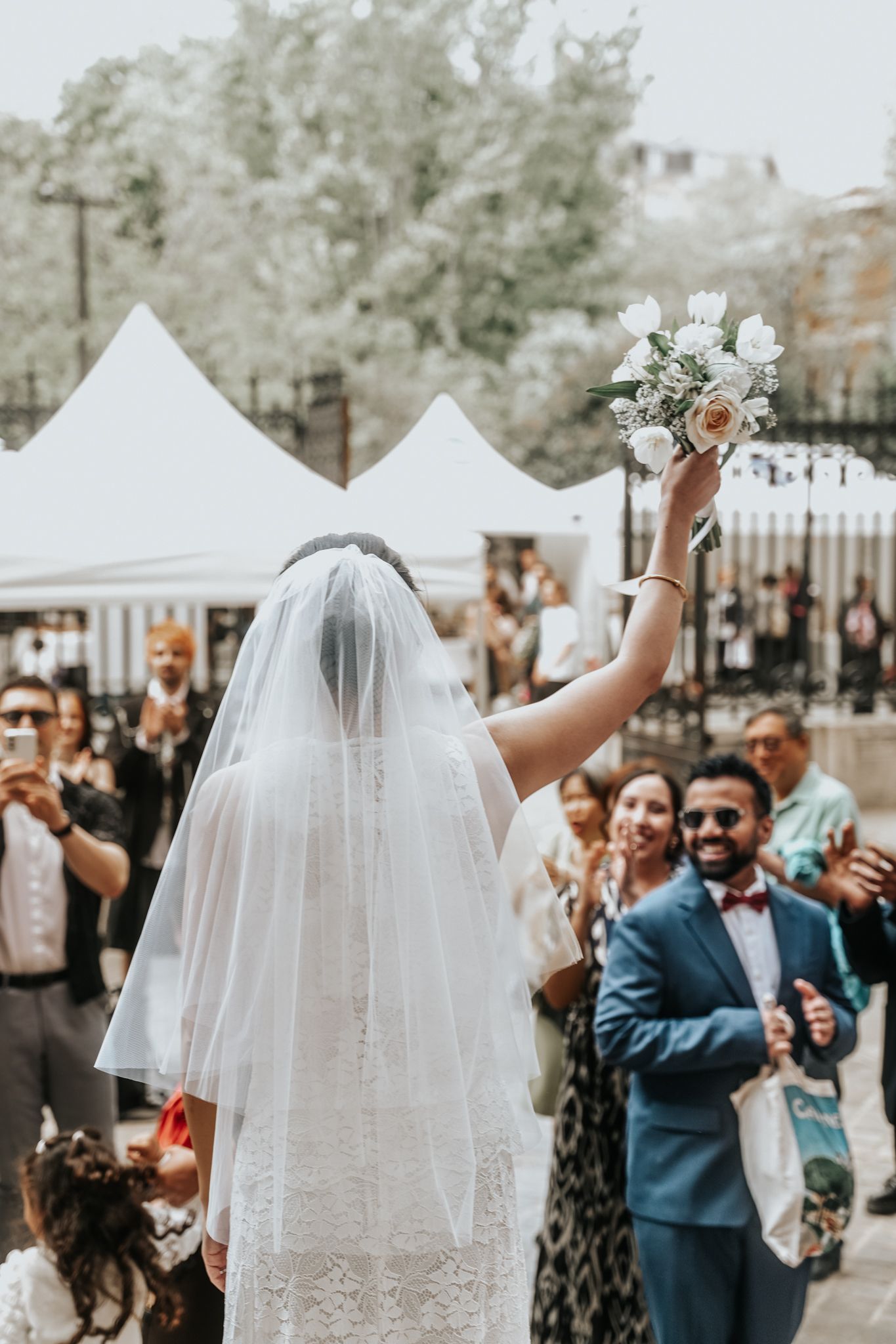 Les invités du mariage célèbrent à l'extérieur sous des tentes blanches les mains levées.