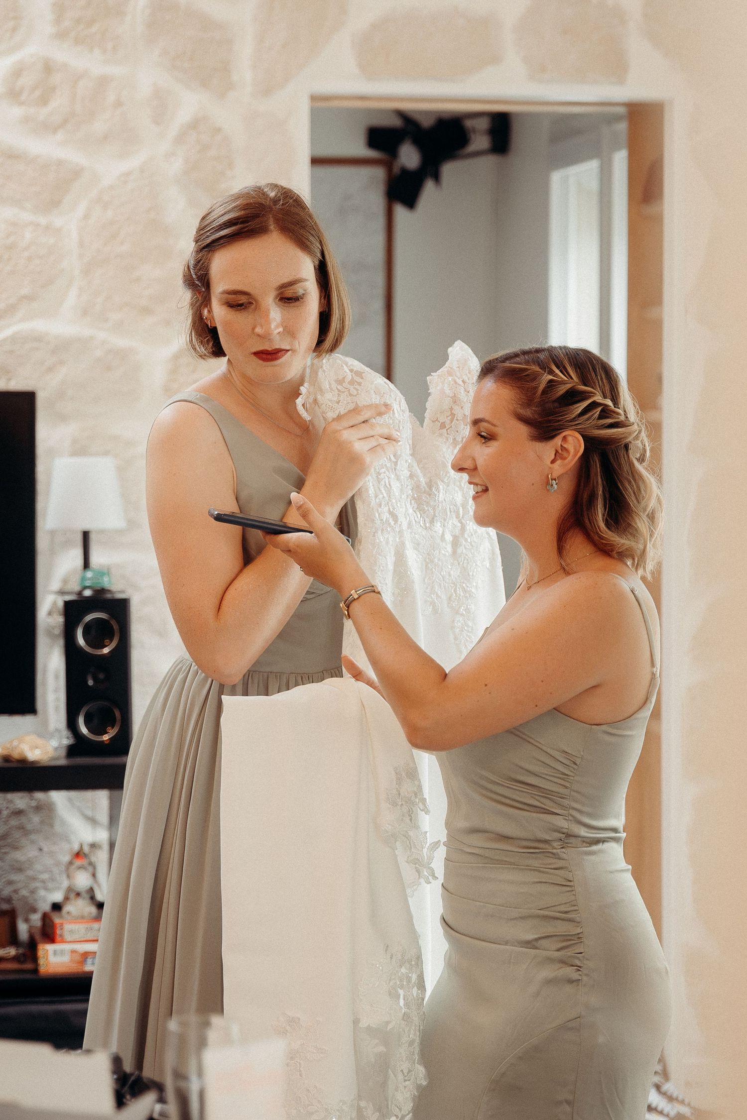 Two women in gray dresses help with a white wedding gown during preparation for a special occasion.