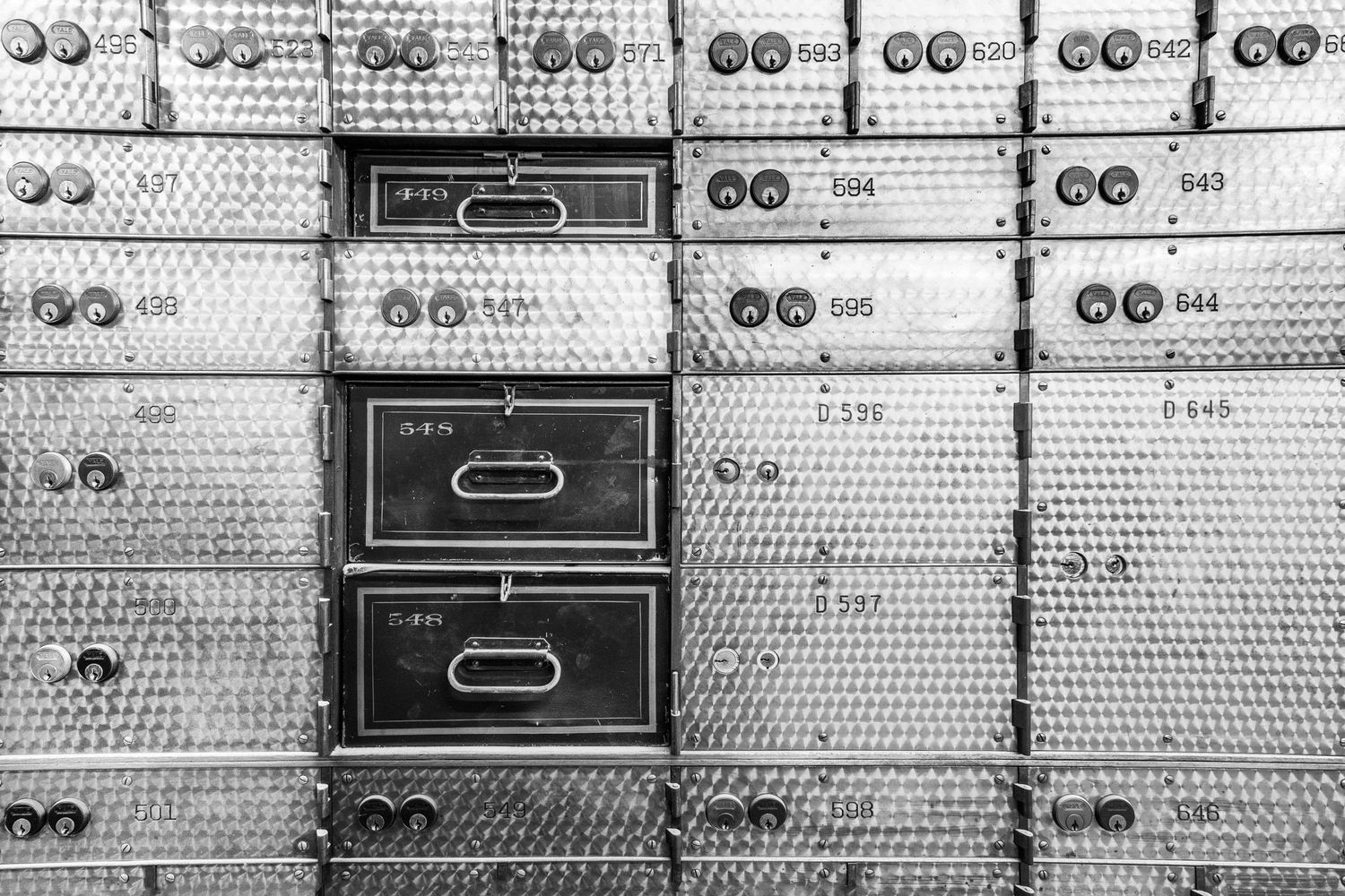 Black and white of vintage safety deposit boxes with numbered plates in a bank vault at the Chrysler House in Detroit, Michigan.