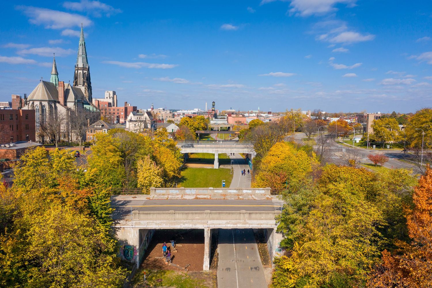 Aerial view of the Dequindre Cut greenway with fall foliage and St Joseph church against a bright blue sky.