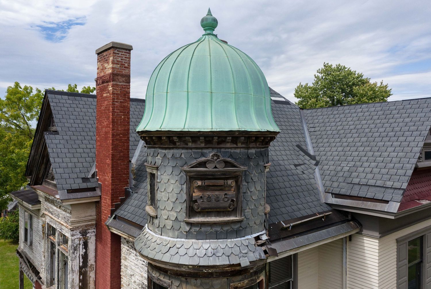 An ornate Victorian-era roofline featuring a copper dome and architectural details with an 1886 plaque at Saginaw, Michigan's Hill House.