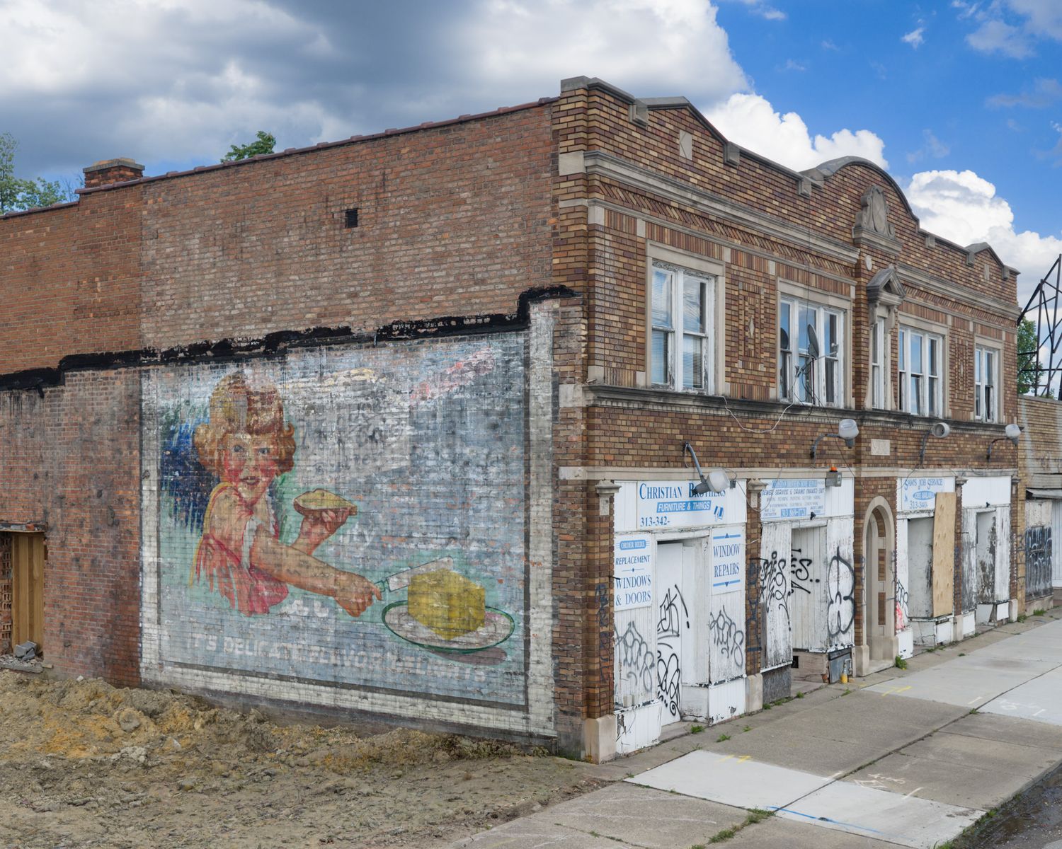 Abandoned brick building corner with colorful mural graffiti art on weathered walls under cloudy sky.